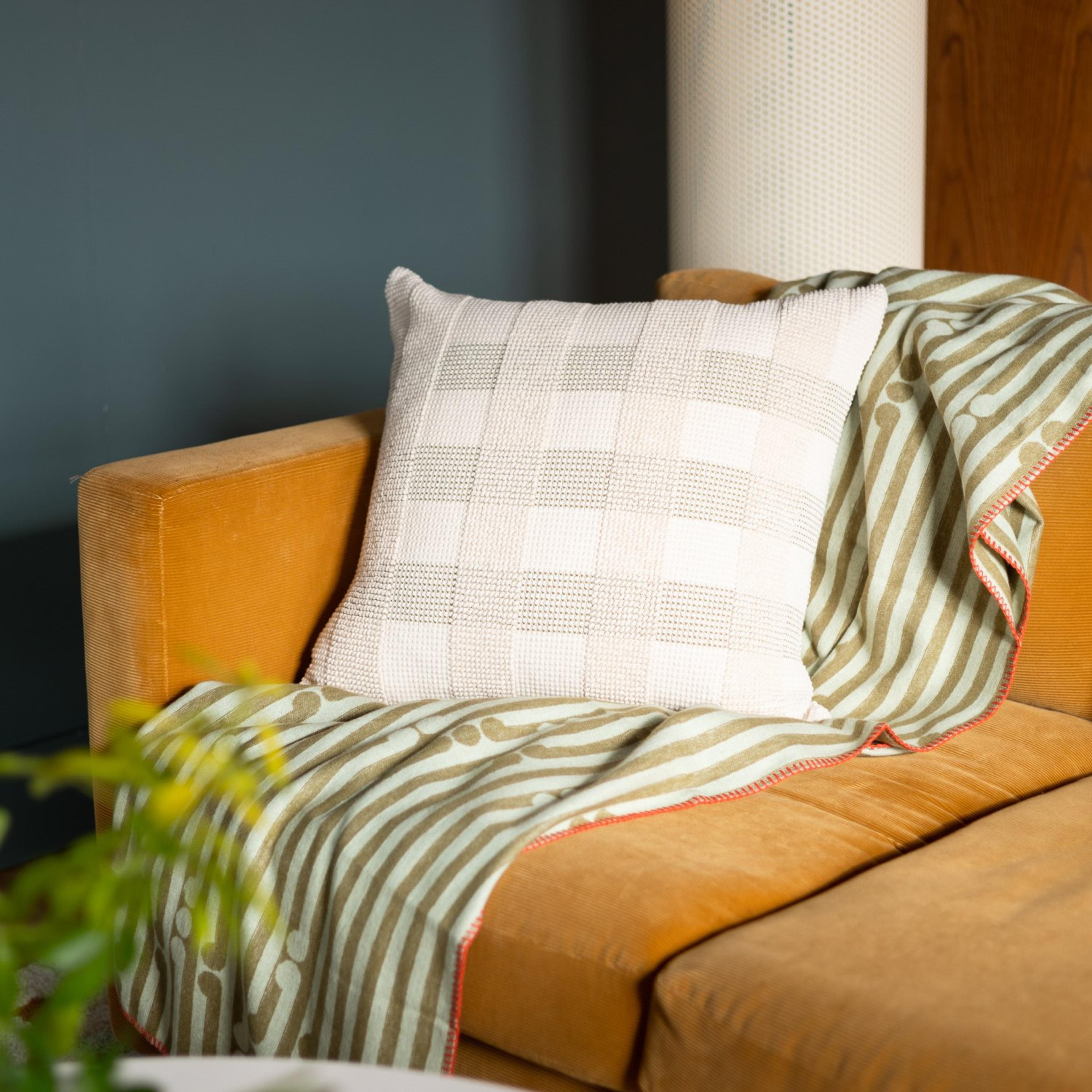 white pillow and green blanket on brown couch