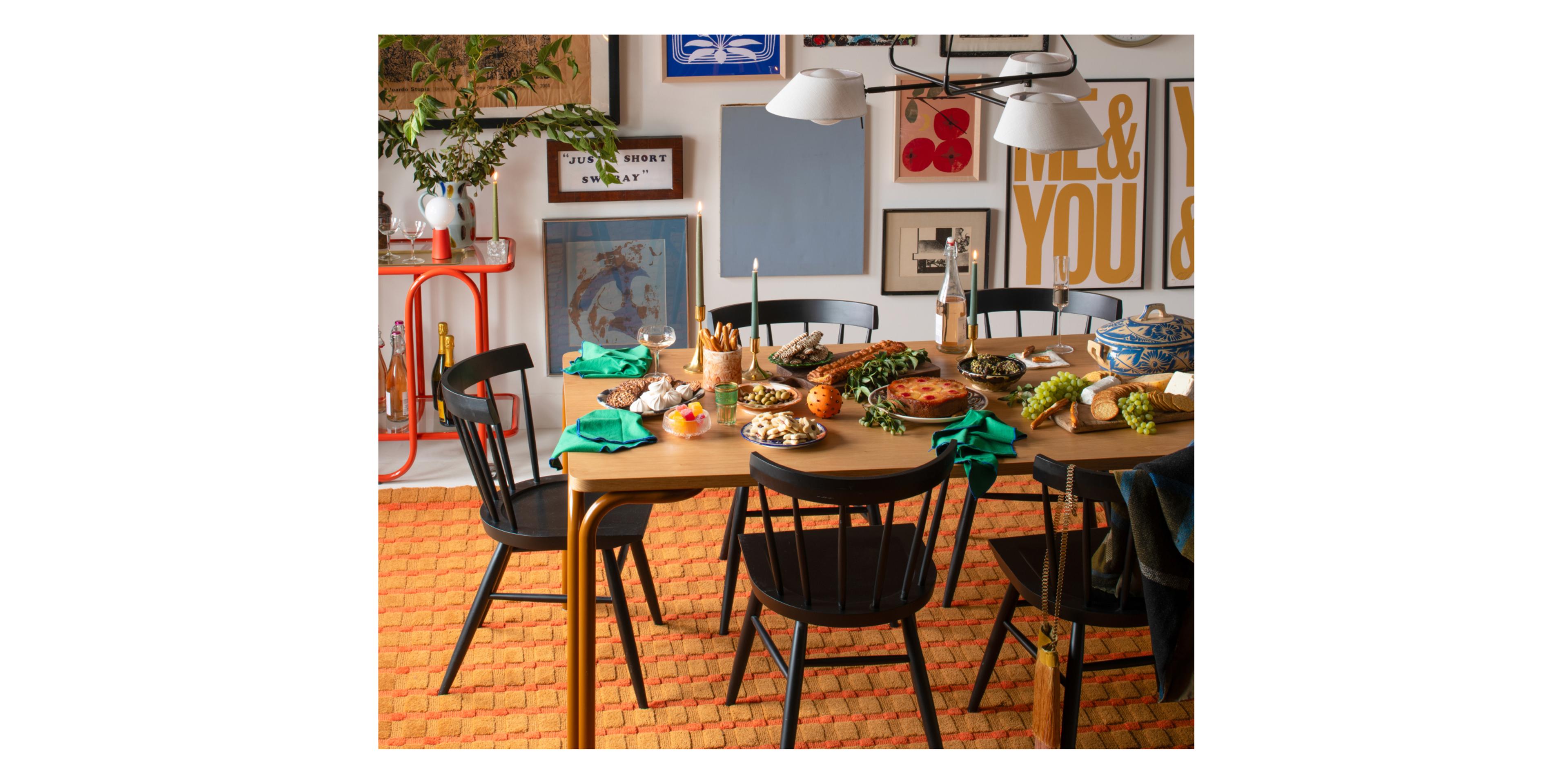 table with butterscotch legs set for holidays with lit candles and gallery wall behind table