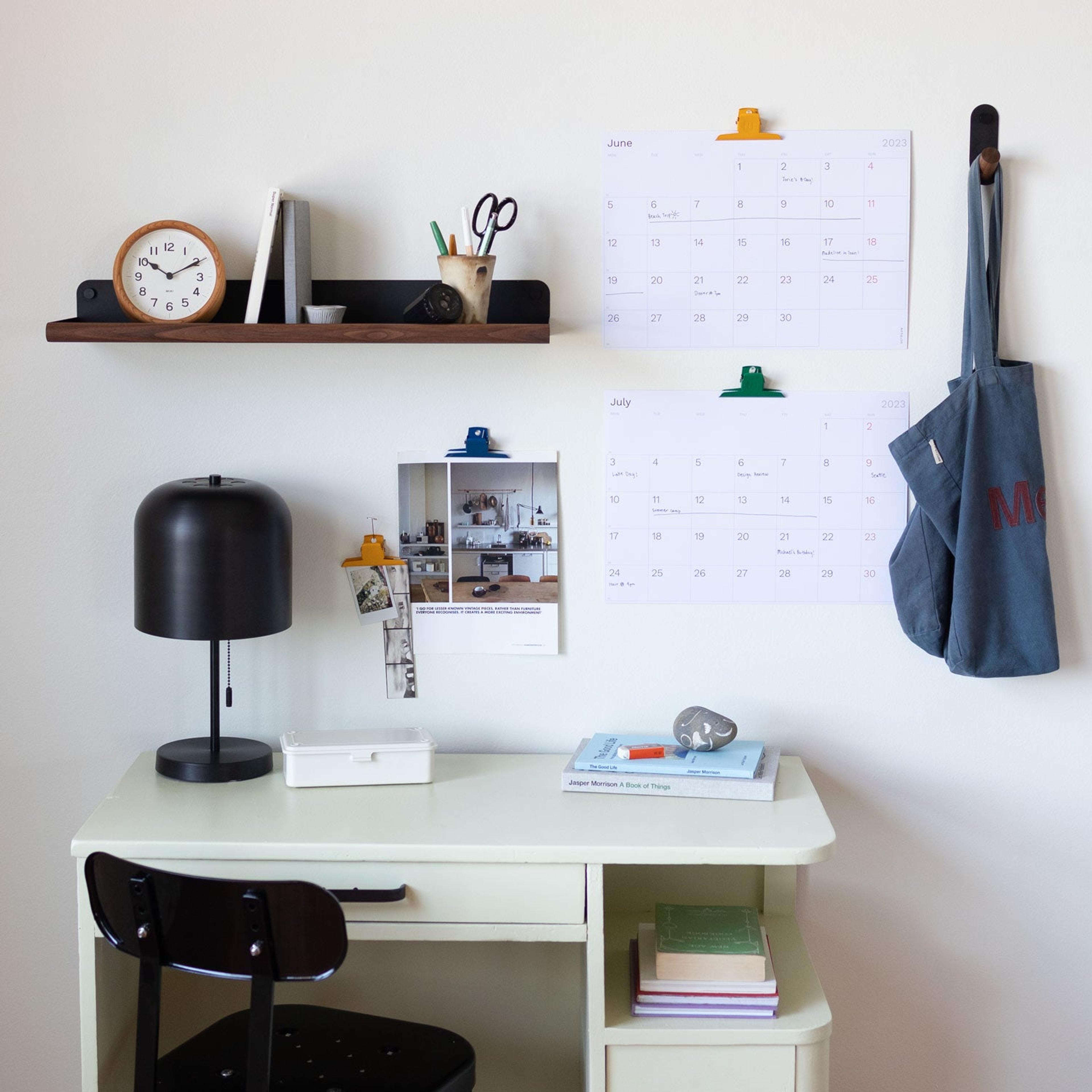 desk space with black metal table lamp and yellow clock overhead