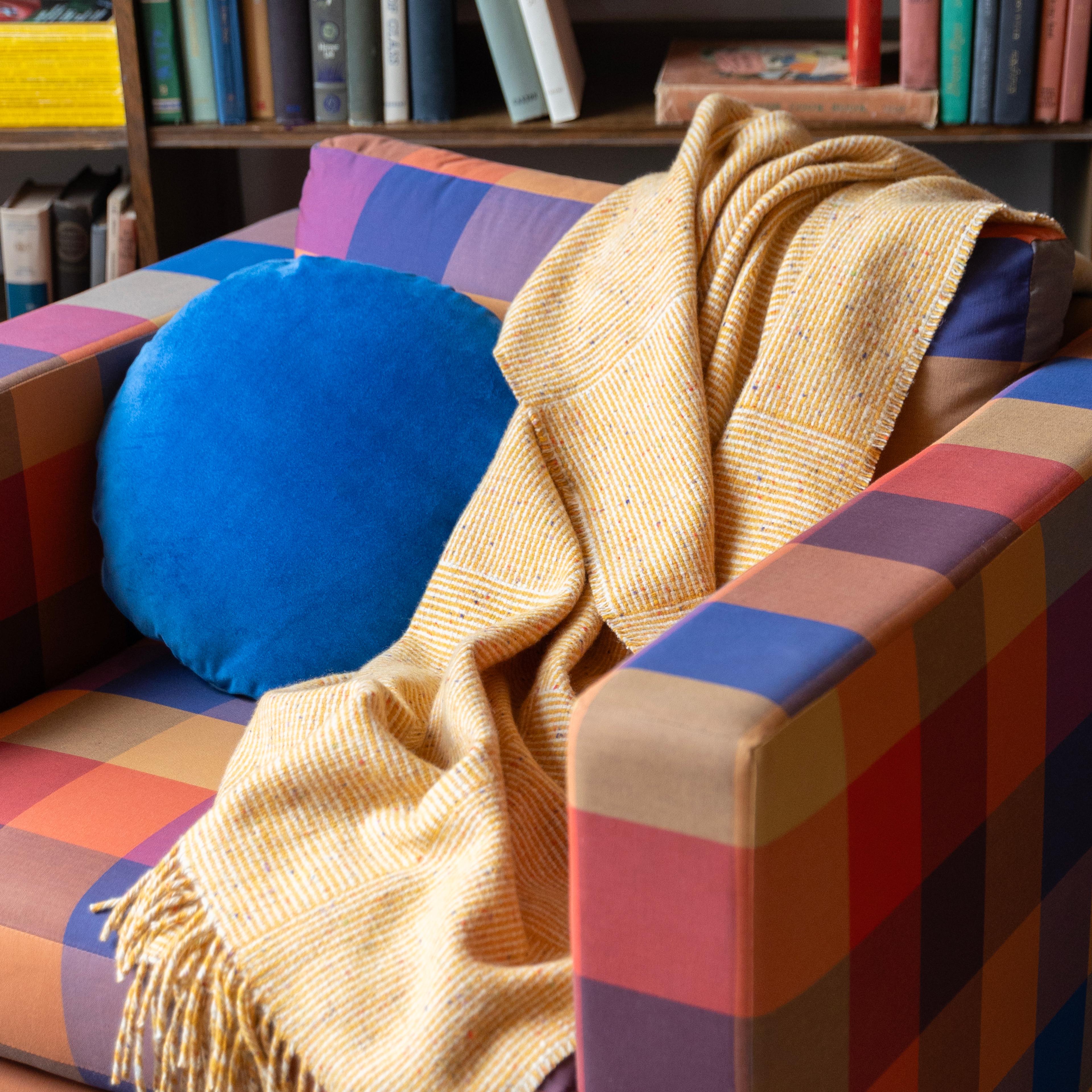 Plaid couch with yellow throw blanket and blue velvet circle pillow