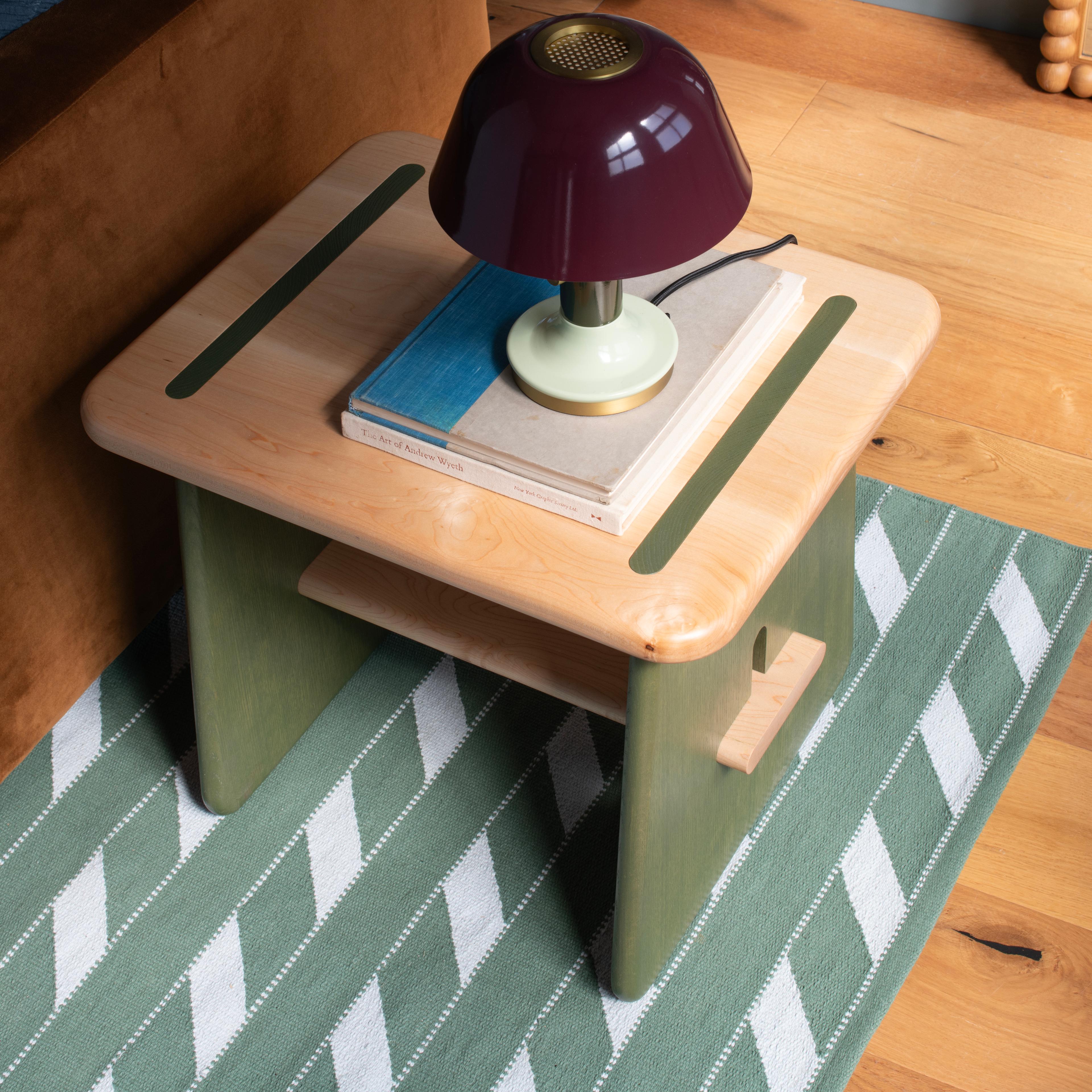 Close-up of wooden side table holding books and a lamp.