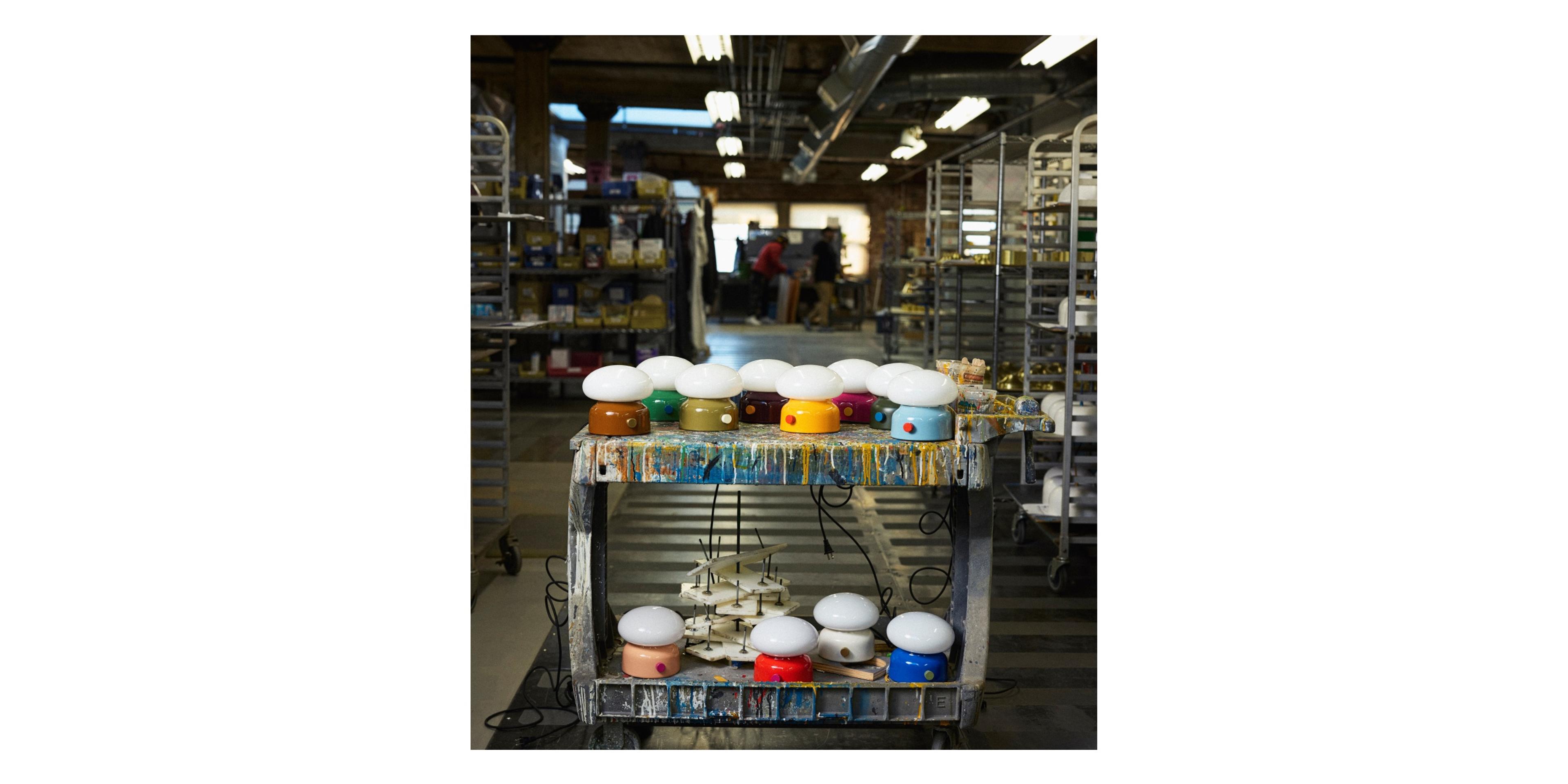 set of multi-colored table lamps on paint cart in middle of paint floor of factory