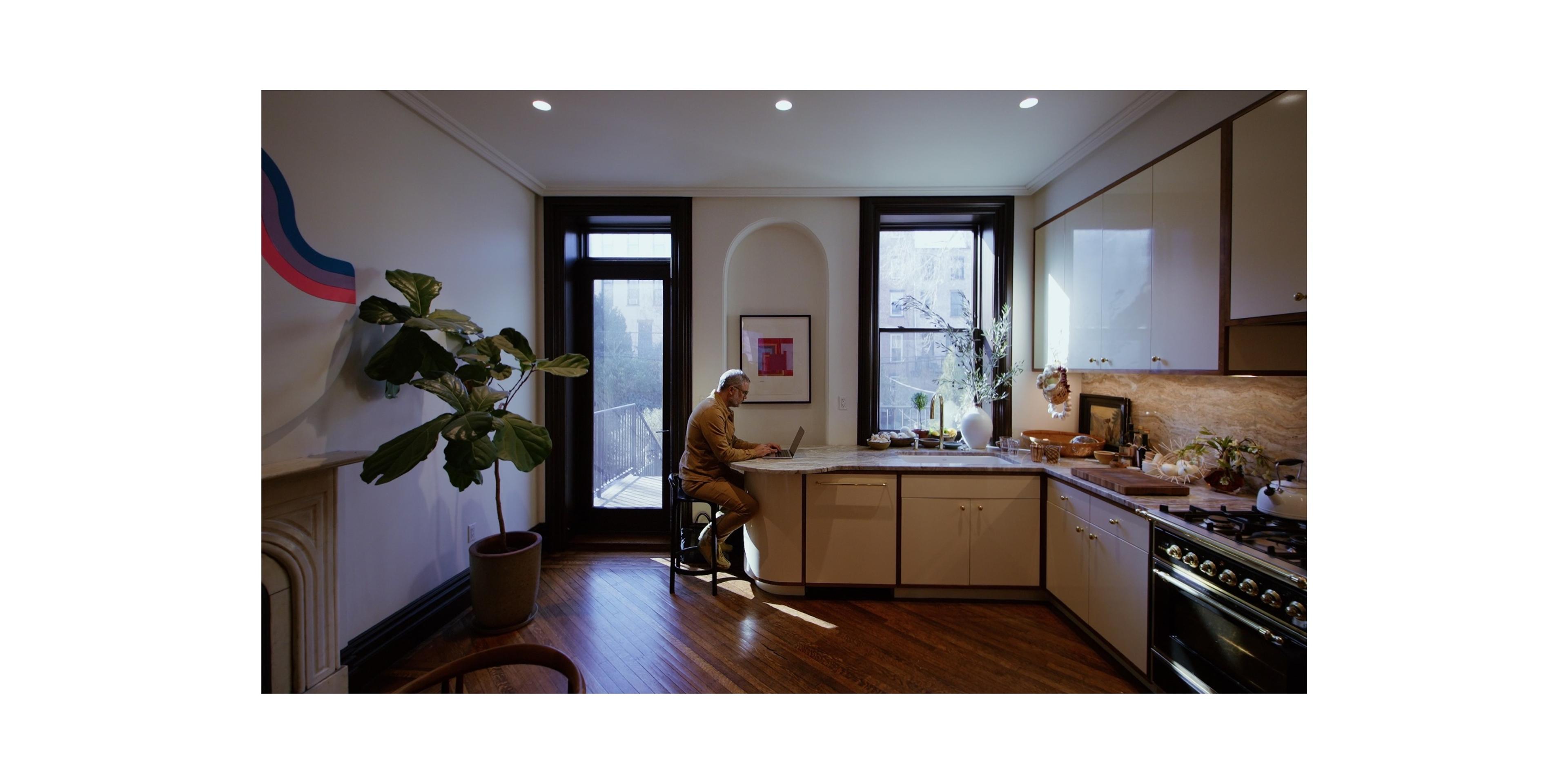 Apartment kitchen with large windows and man sitting at countertop working on laptop