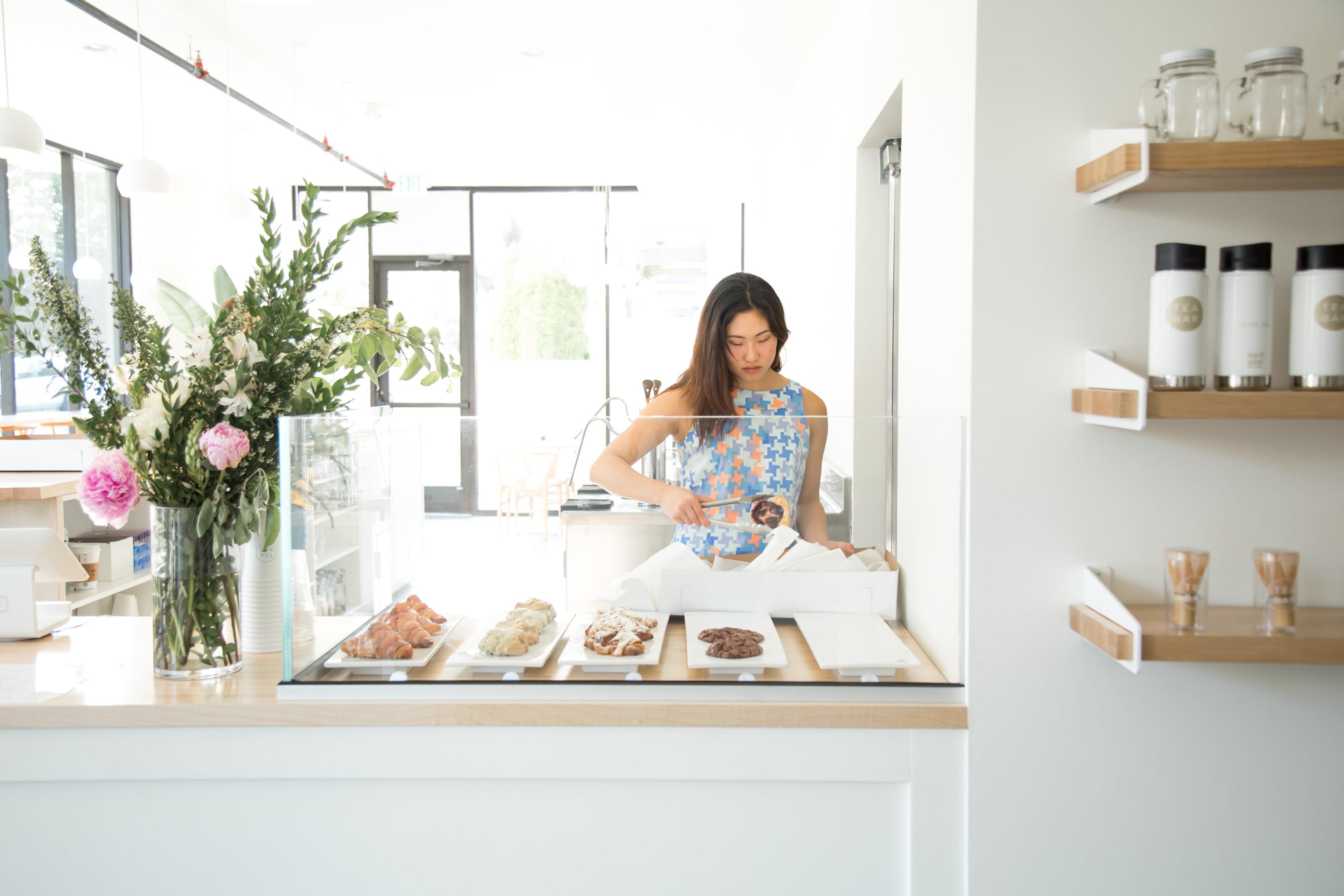 person standing behind a counter with pastries in a glass case