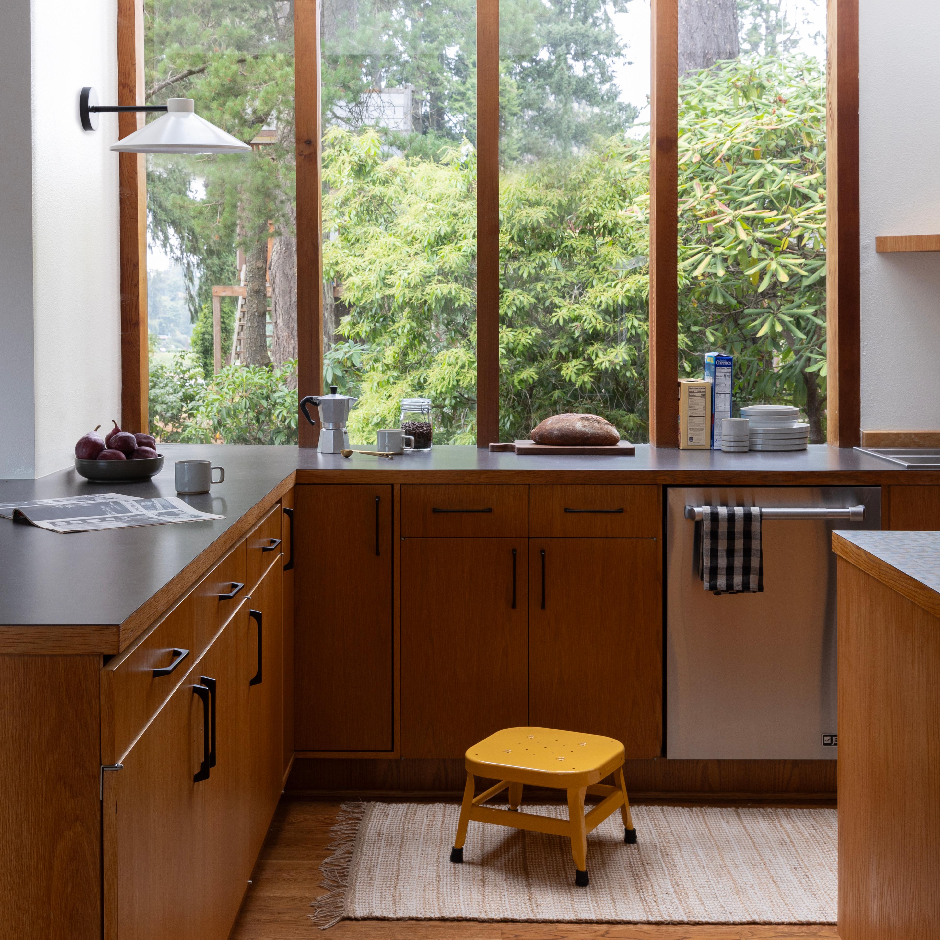 Modern kitchen with large windows overlooking forestry and yellow step stool in front of dishwasher