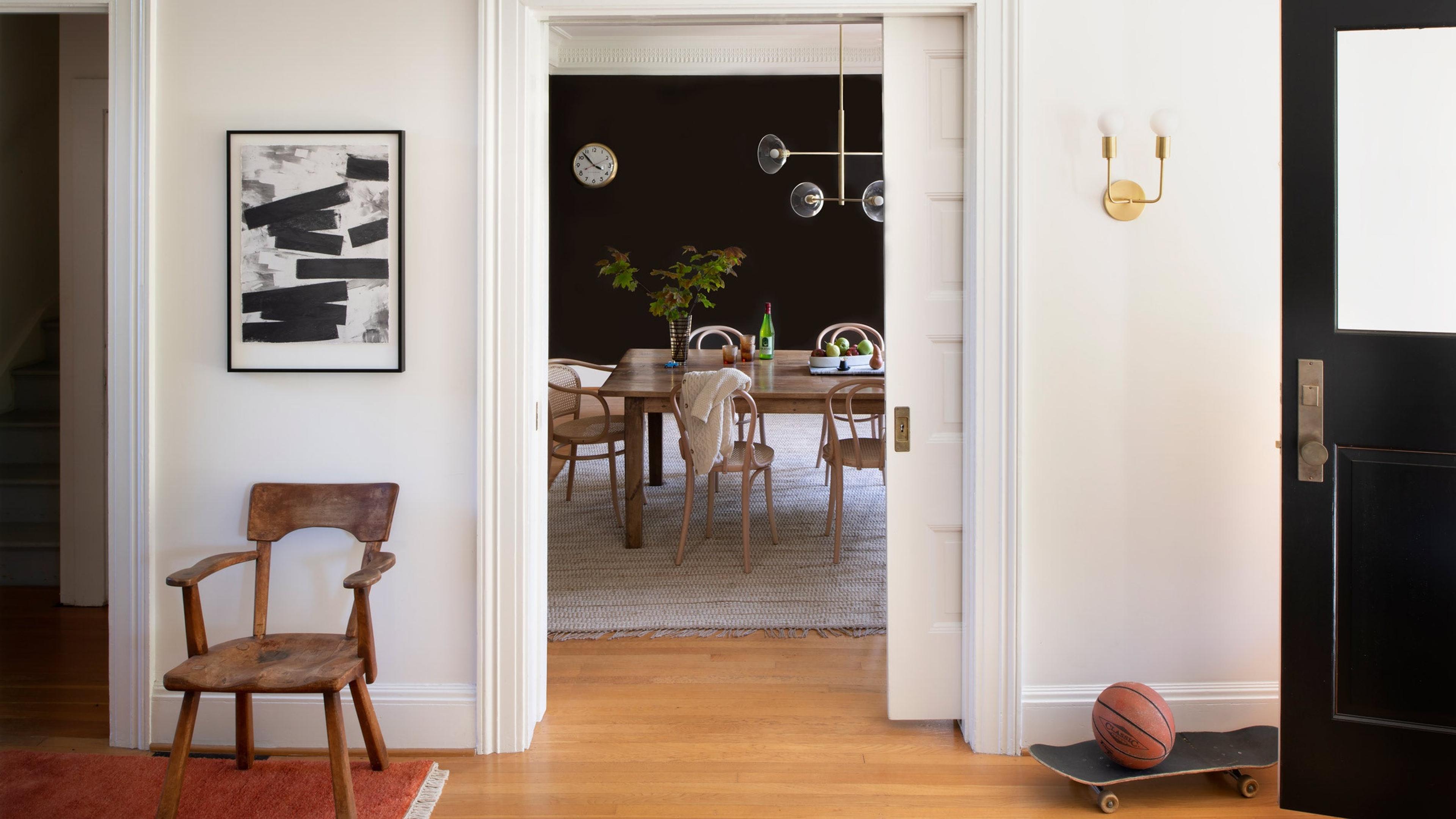 An entryway looking into a dining room with a brass chandelier.
