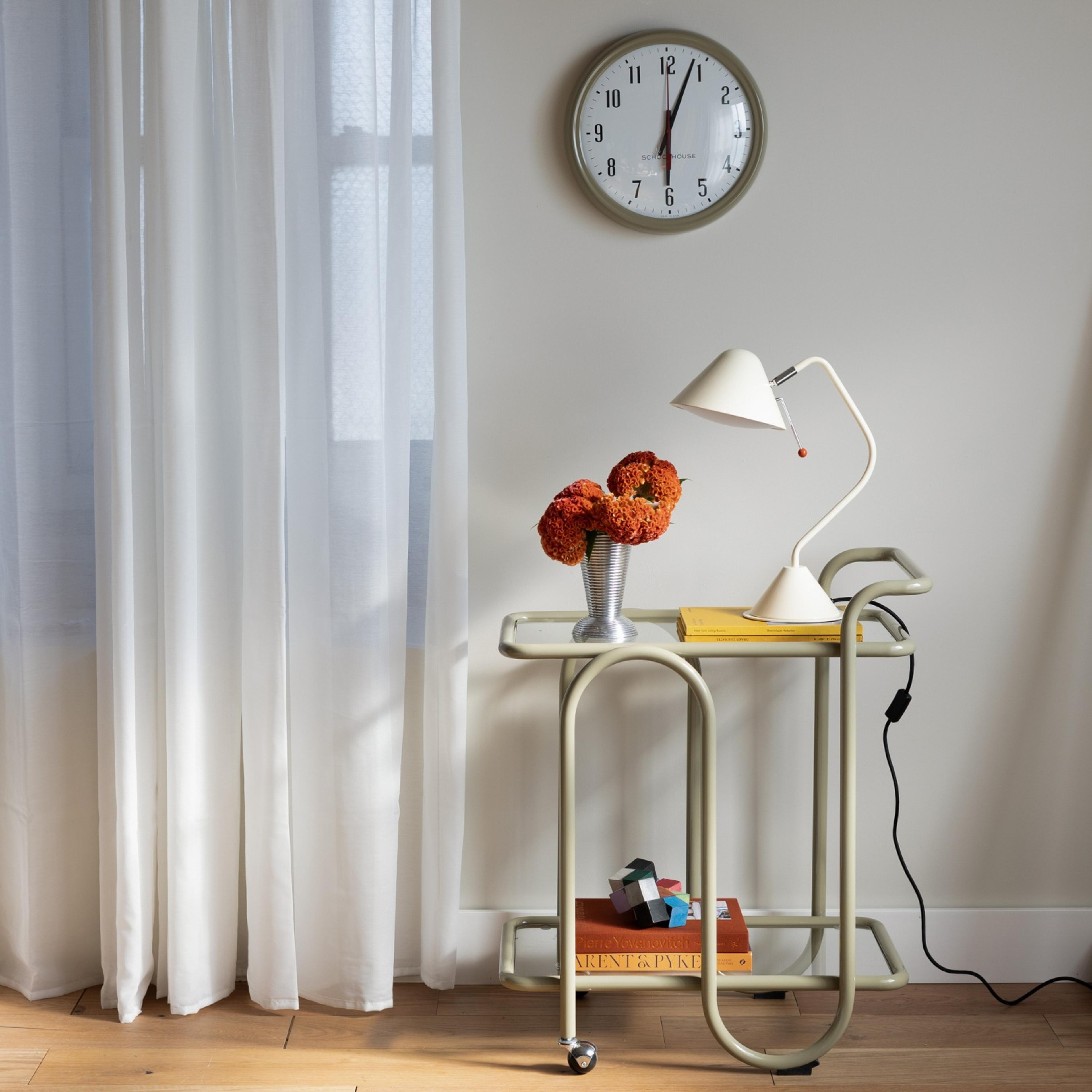 Bar cart with a table lamp and books on it, clock above it