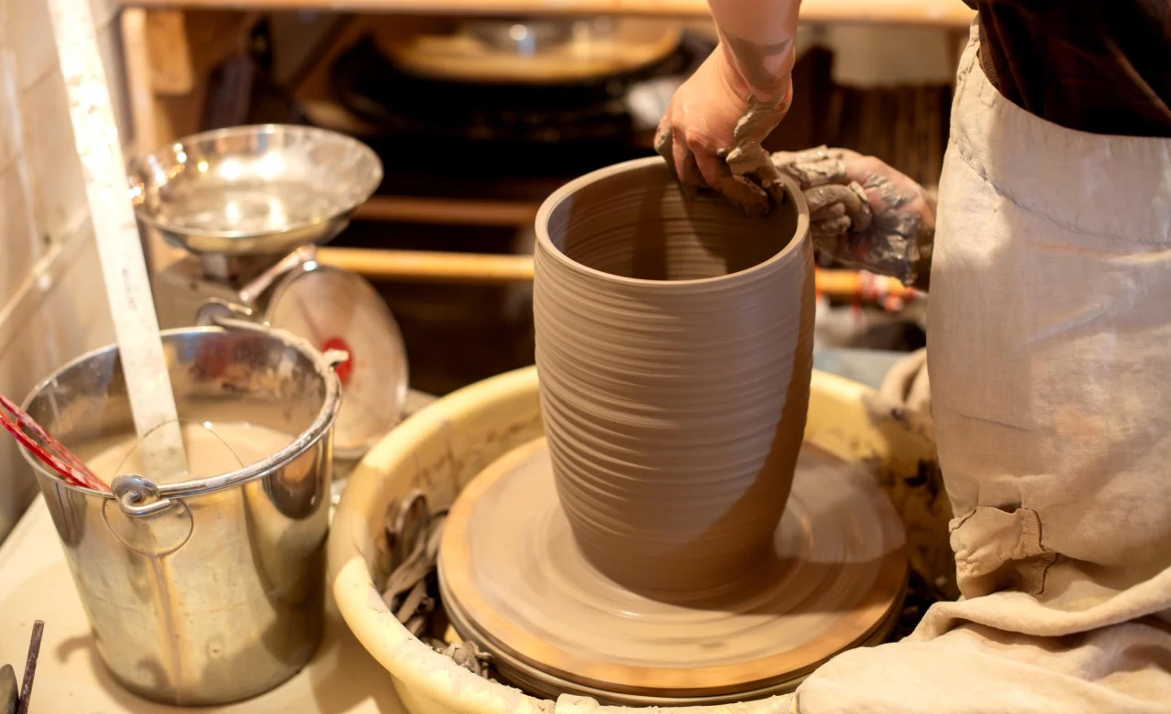 A clay vase with ridges on the side being shaped by a hand