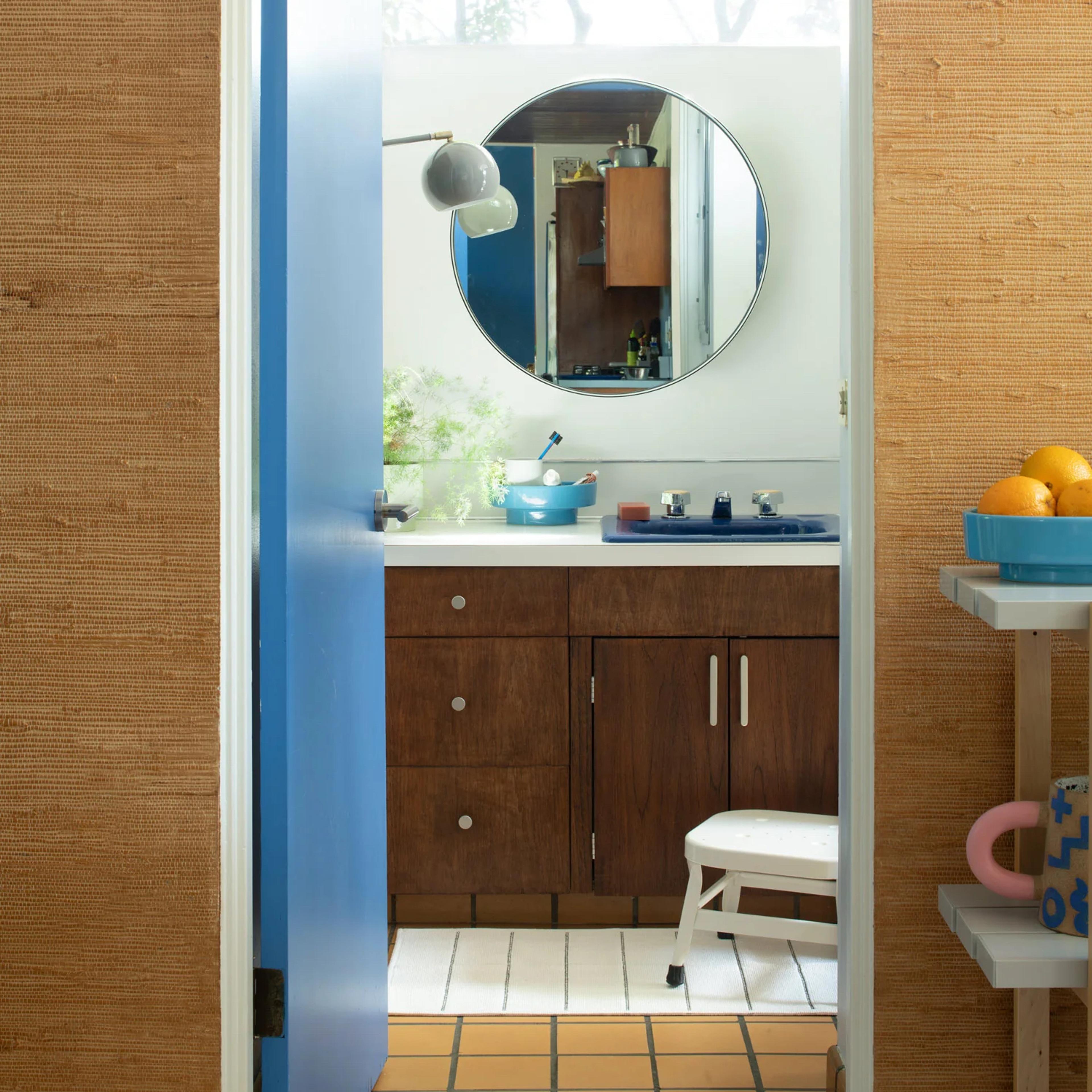 Bathroom entry with blue door and light green lighting over round mirror