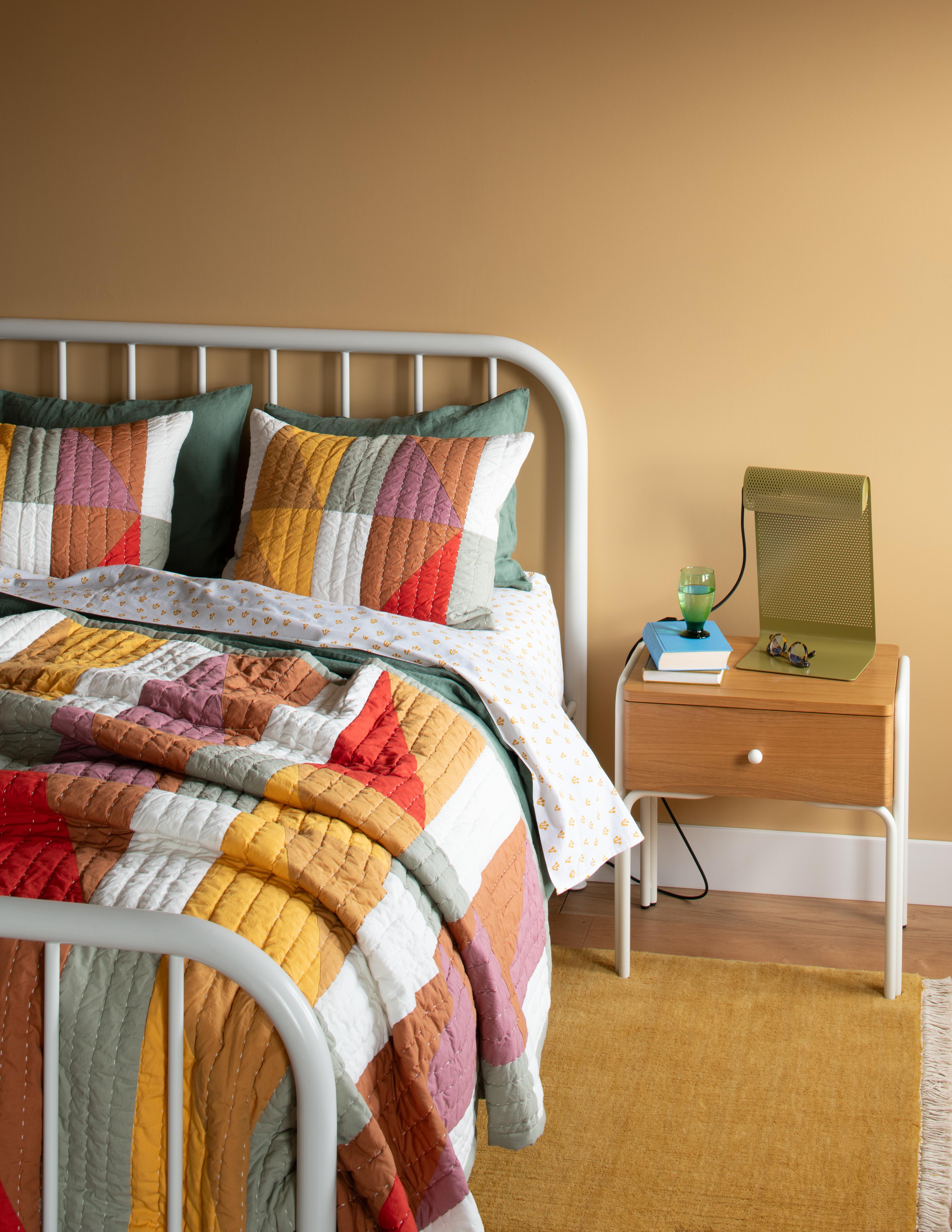 perforated table lamp lit up on night stand next to bed with colorful quilt