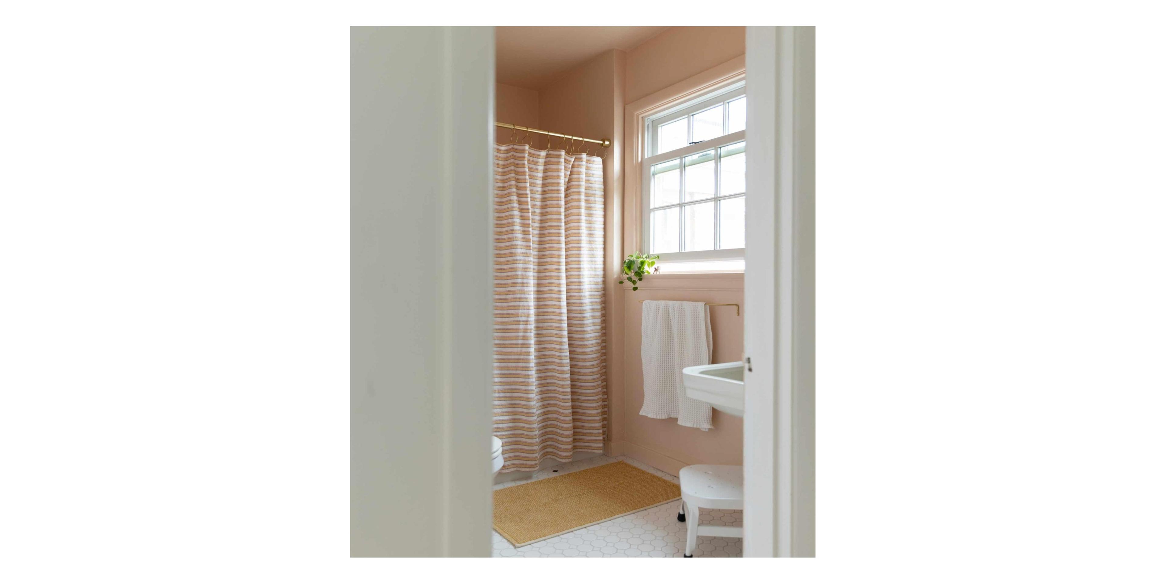 Pink bathroom with striped shower curtain and yellow bath mat.