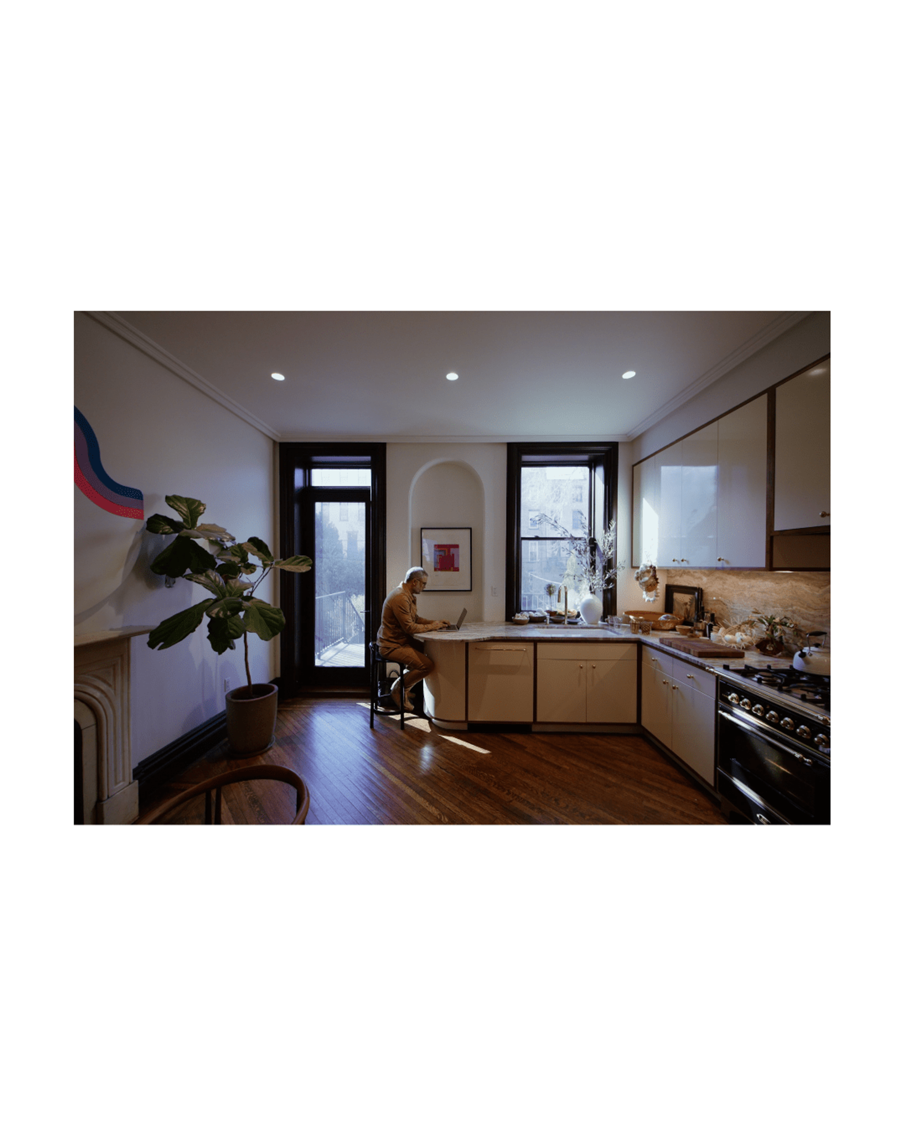 Apartment kitchen with large windows and man sitting at countertop working on laptop