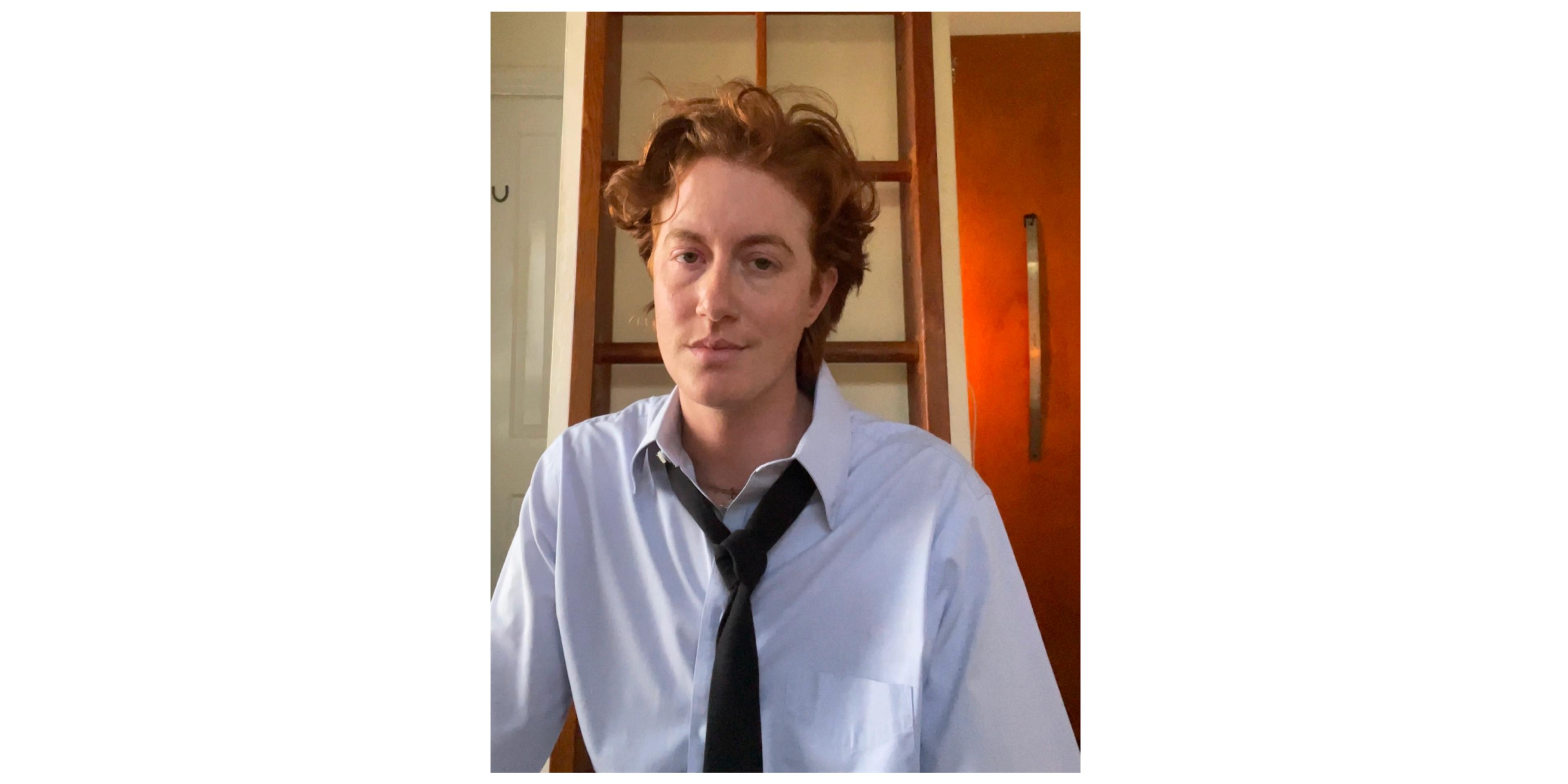 Headshot of person with red hair and blue button up with black tie 