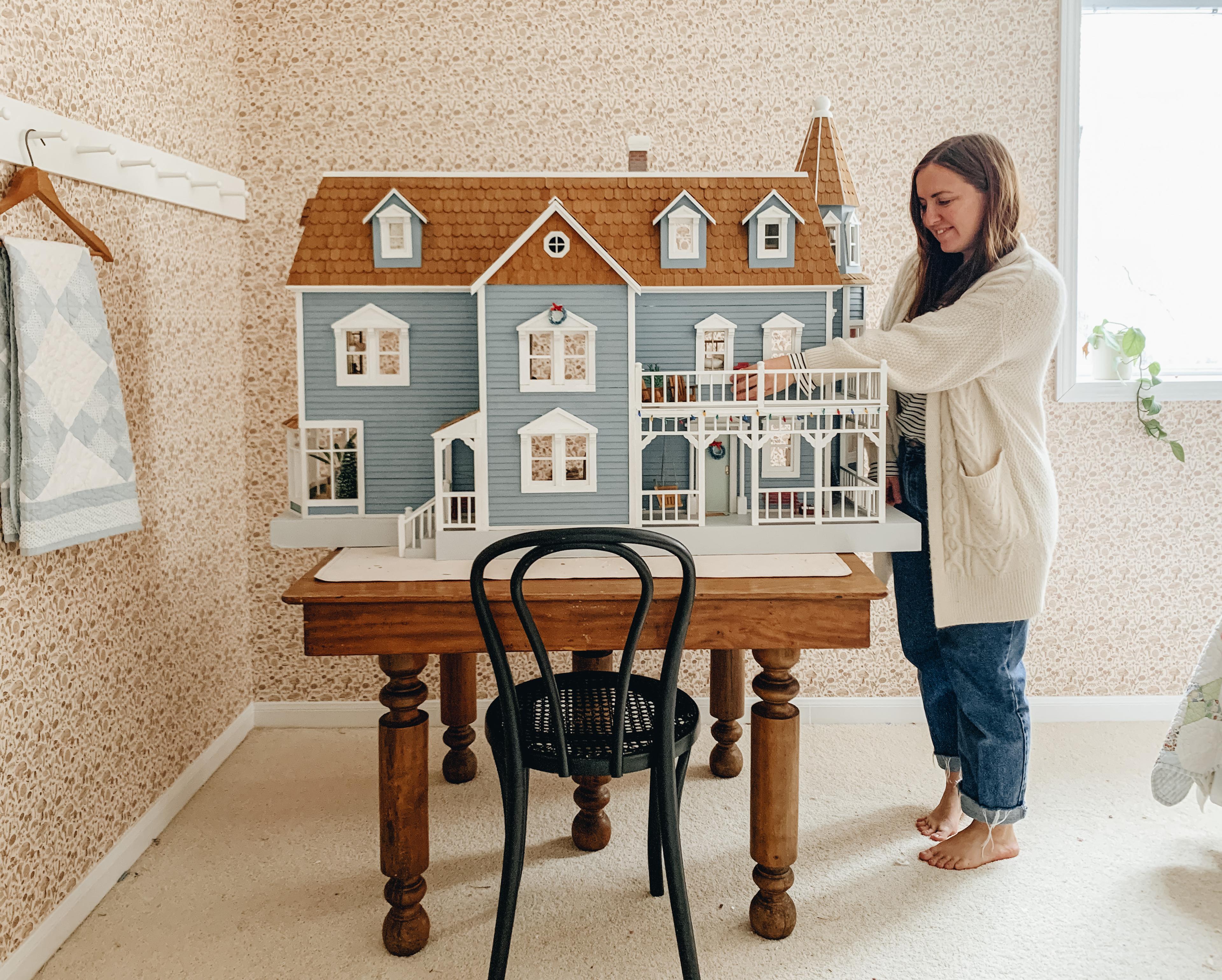 Woman standing next to dollhouse.