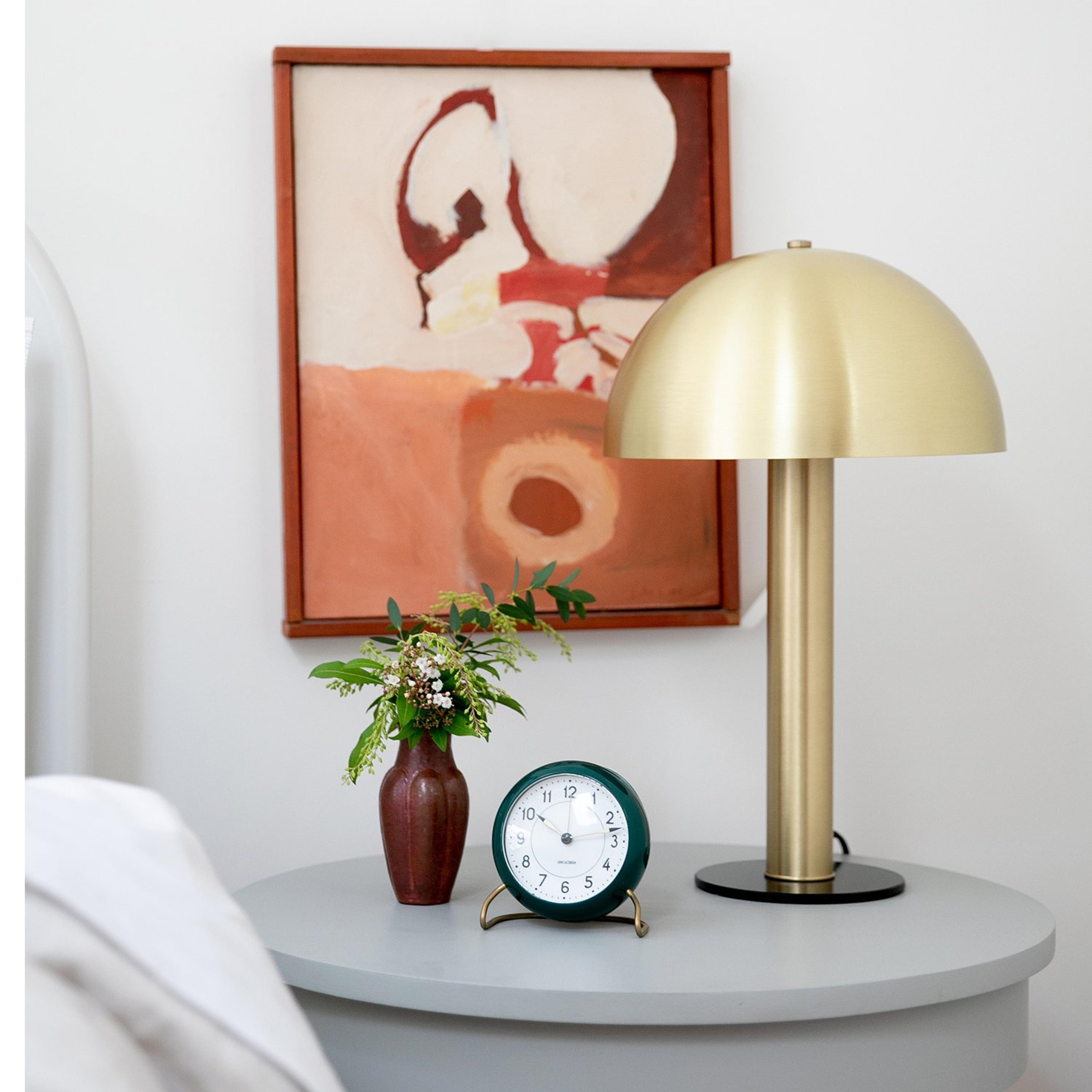 Brass mushroom shaped lamp on bedside table with small plant and analog alarm clock