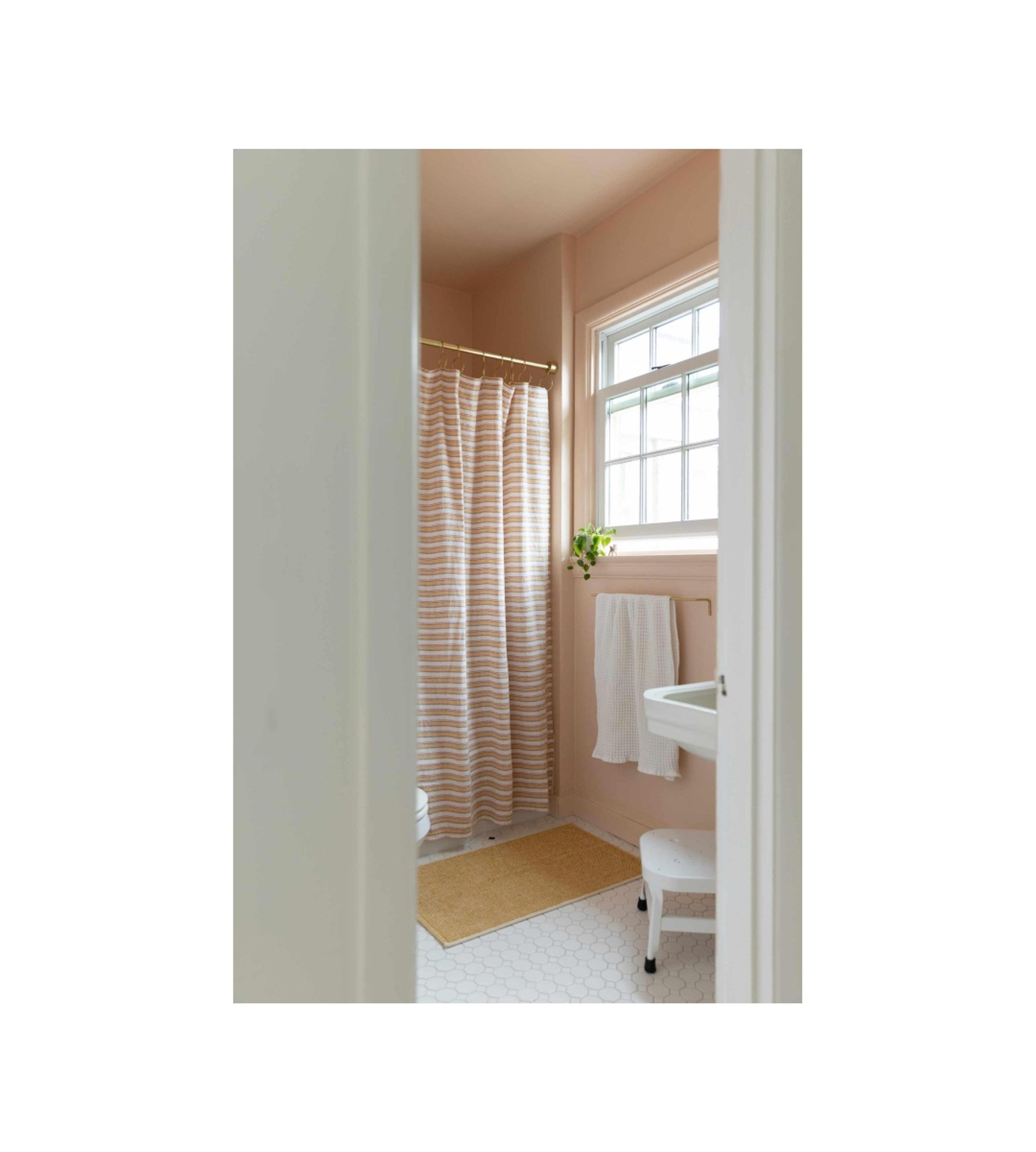 Pink bathroom with striped shower curtain and yellow bath mat.