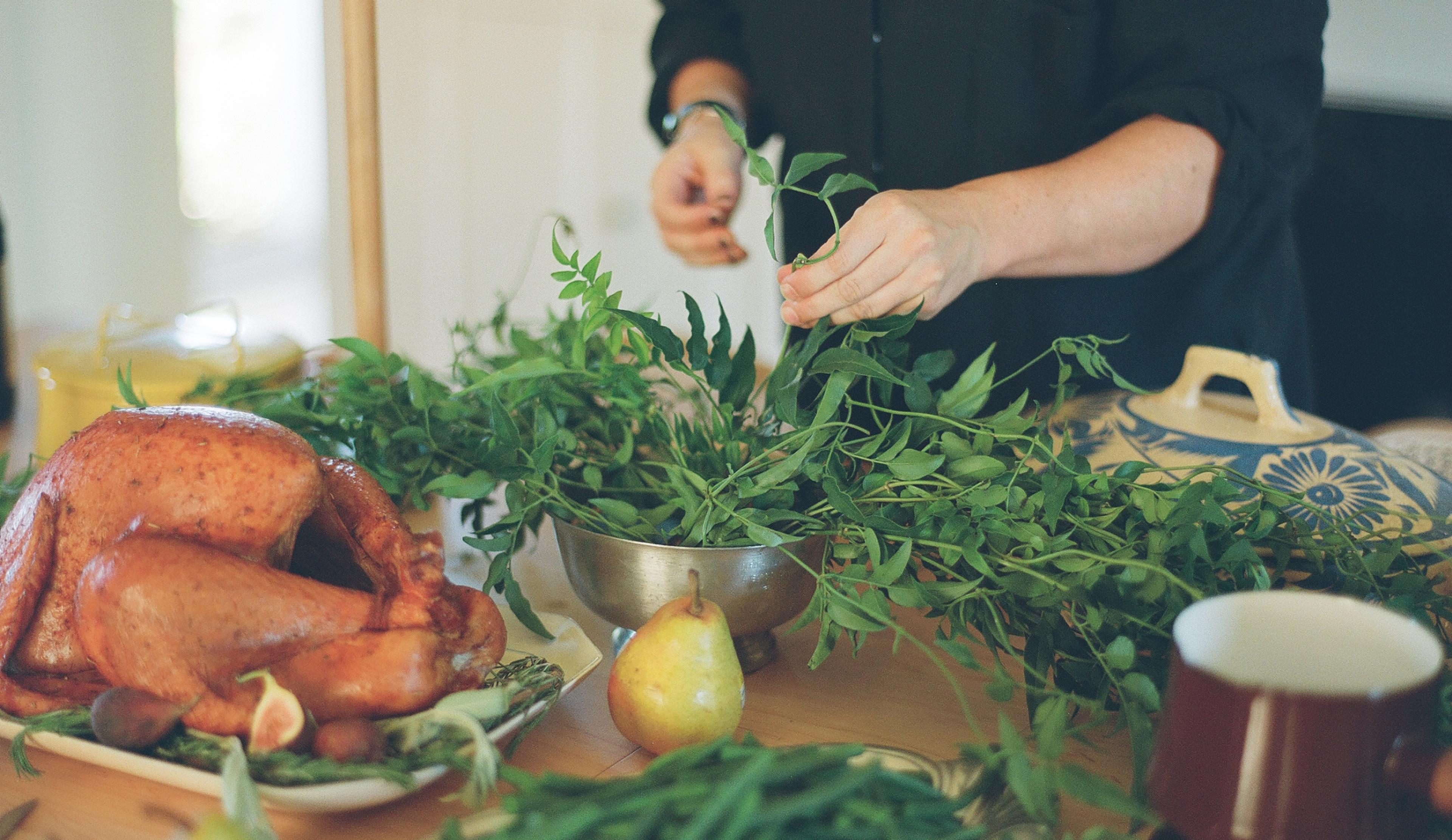 a holiday table being set with a roasted turkey and greenery being arranged