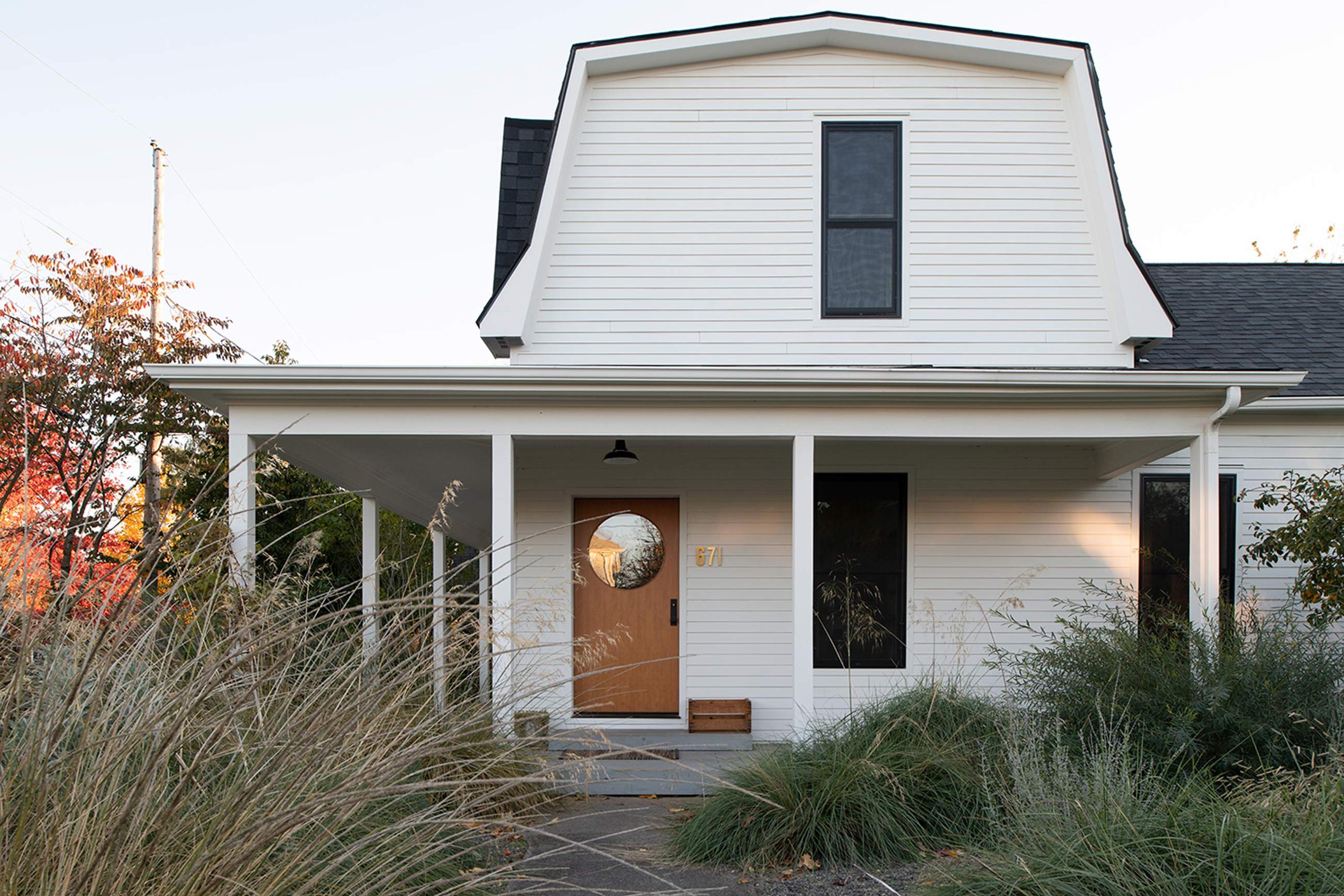 White house with a factory pendant light on the front porch above a wooden door with a round glass window.