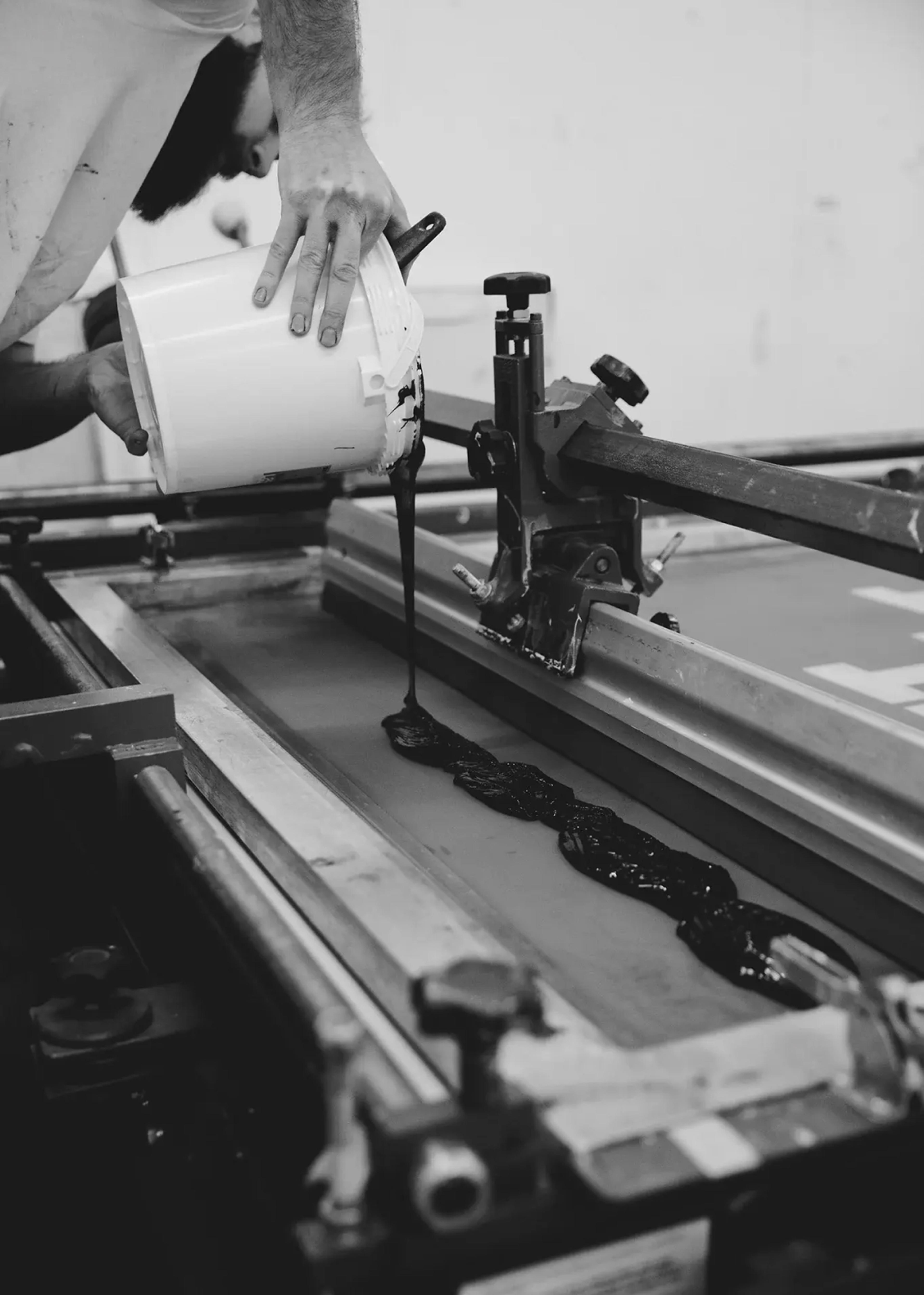 Person pouring paint onto screen printer 