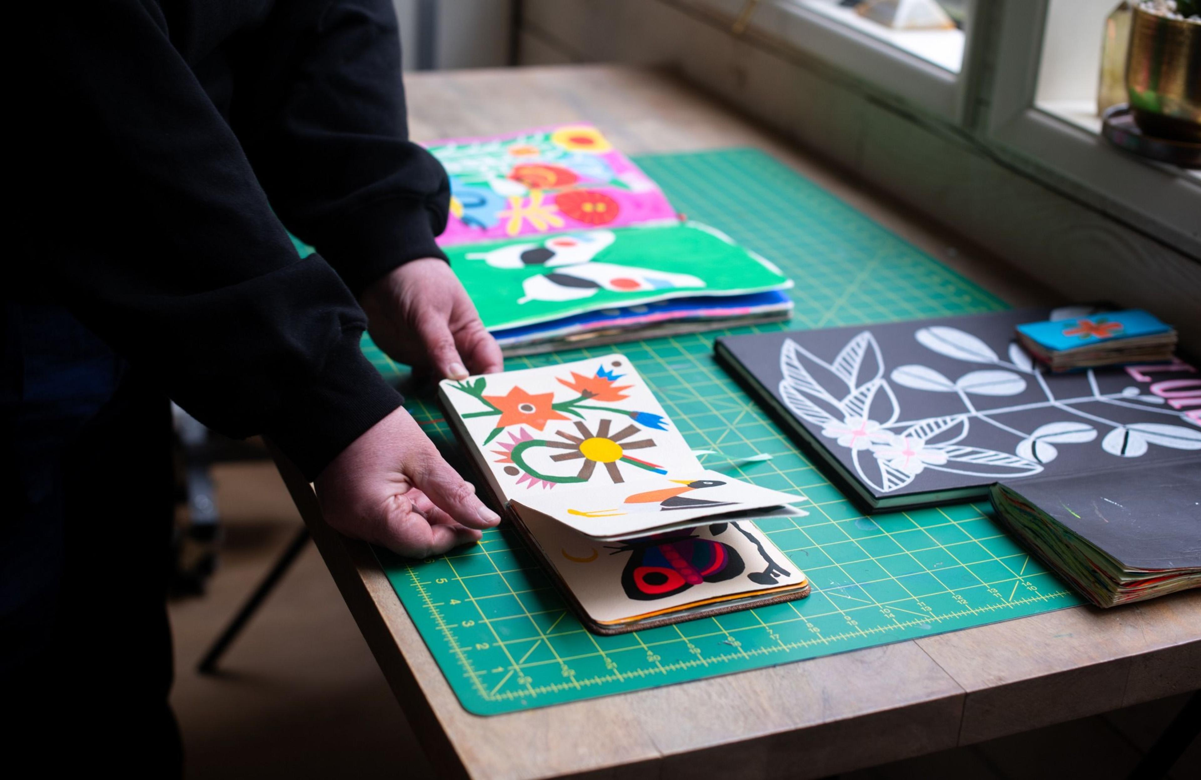 artist browsing through notebook of illustrations on worktable
