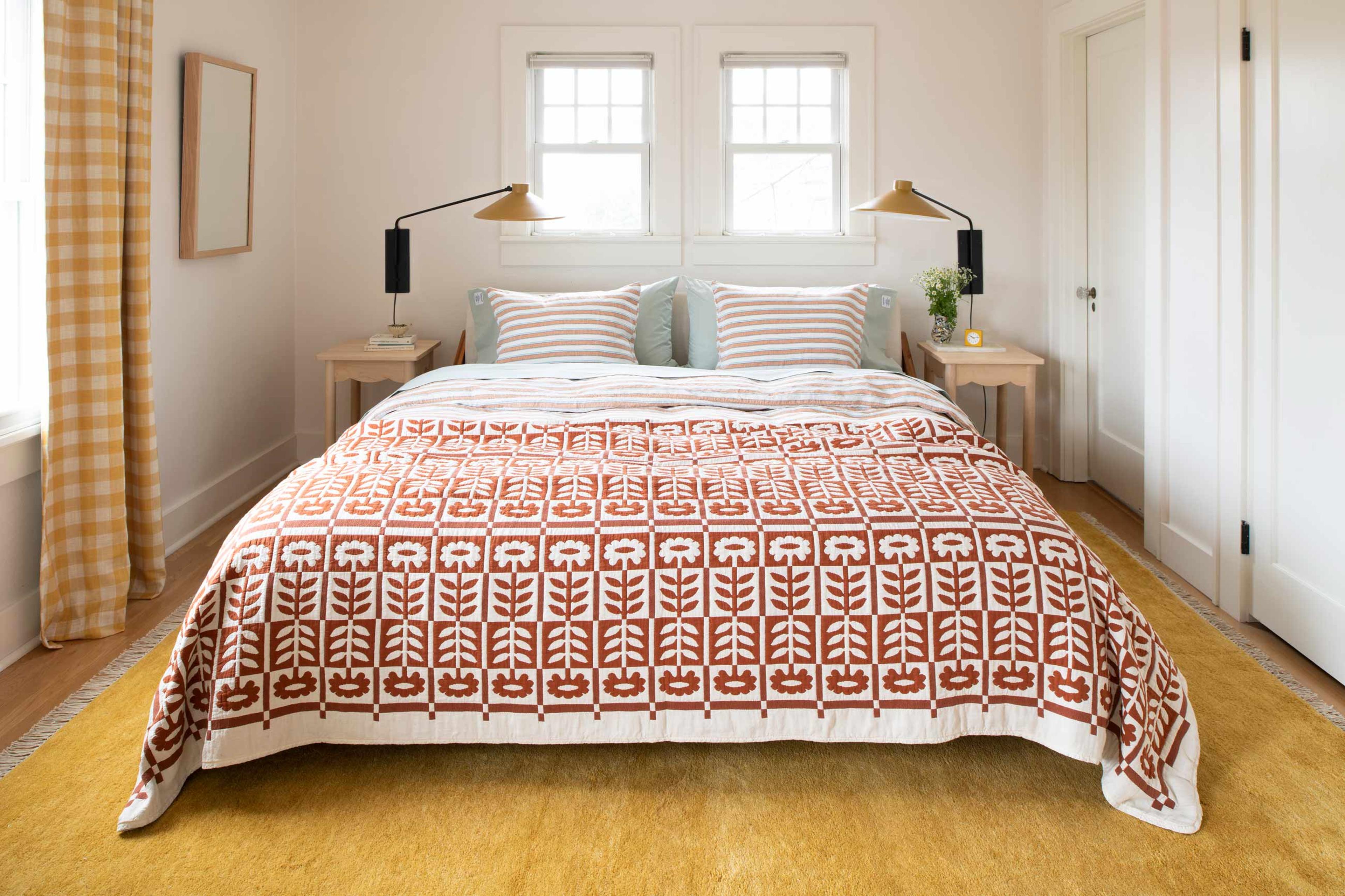 A bedroom with a honey-toned rug, bedside wall sconces, and a floral quilt on a queen-sized bed.