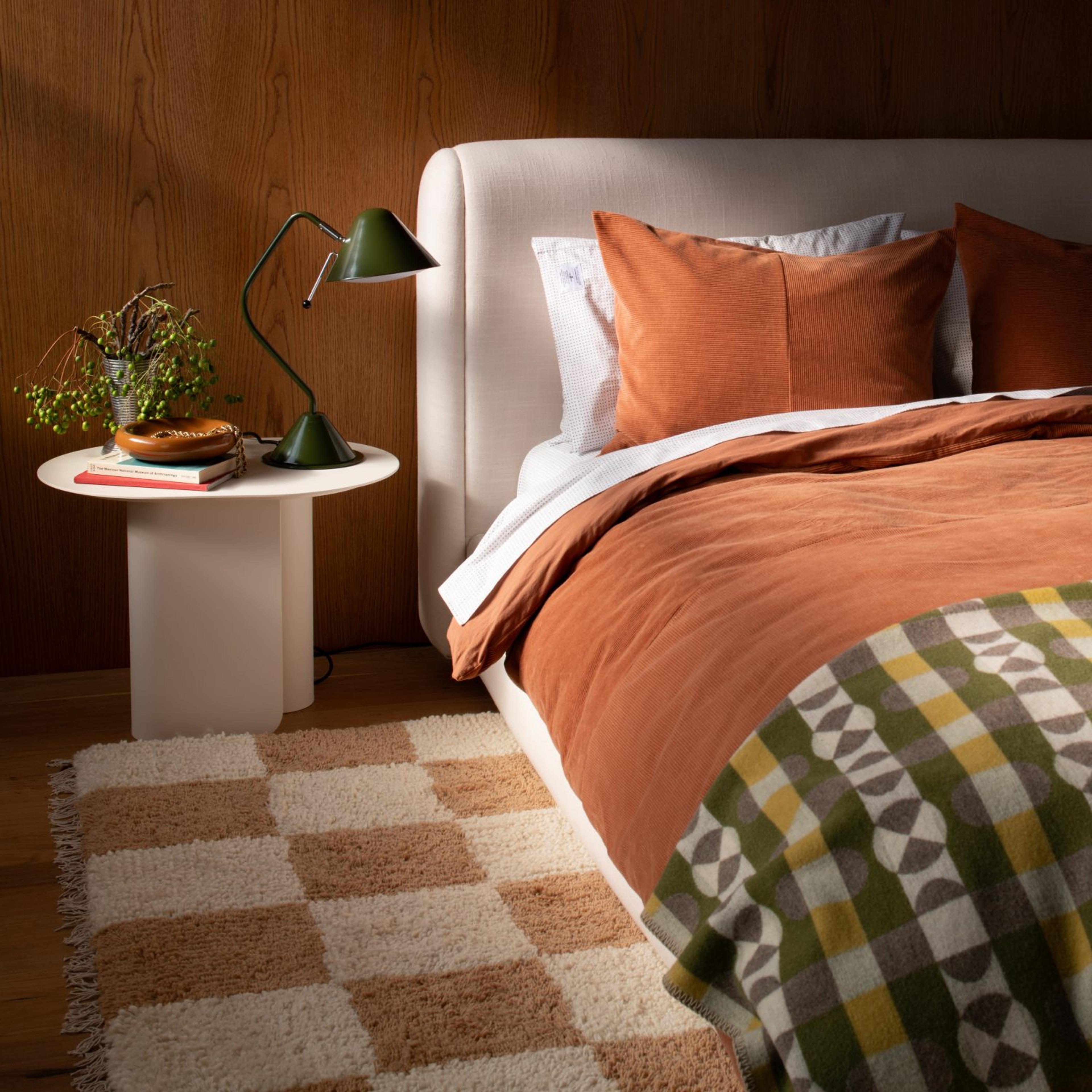 Upholstered bed on top of a checkboard rug with a white side table