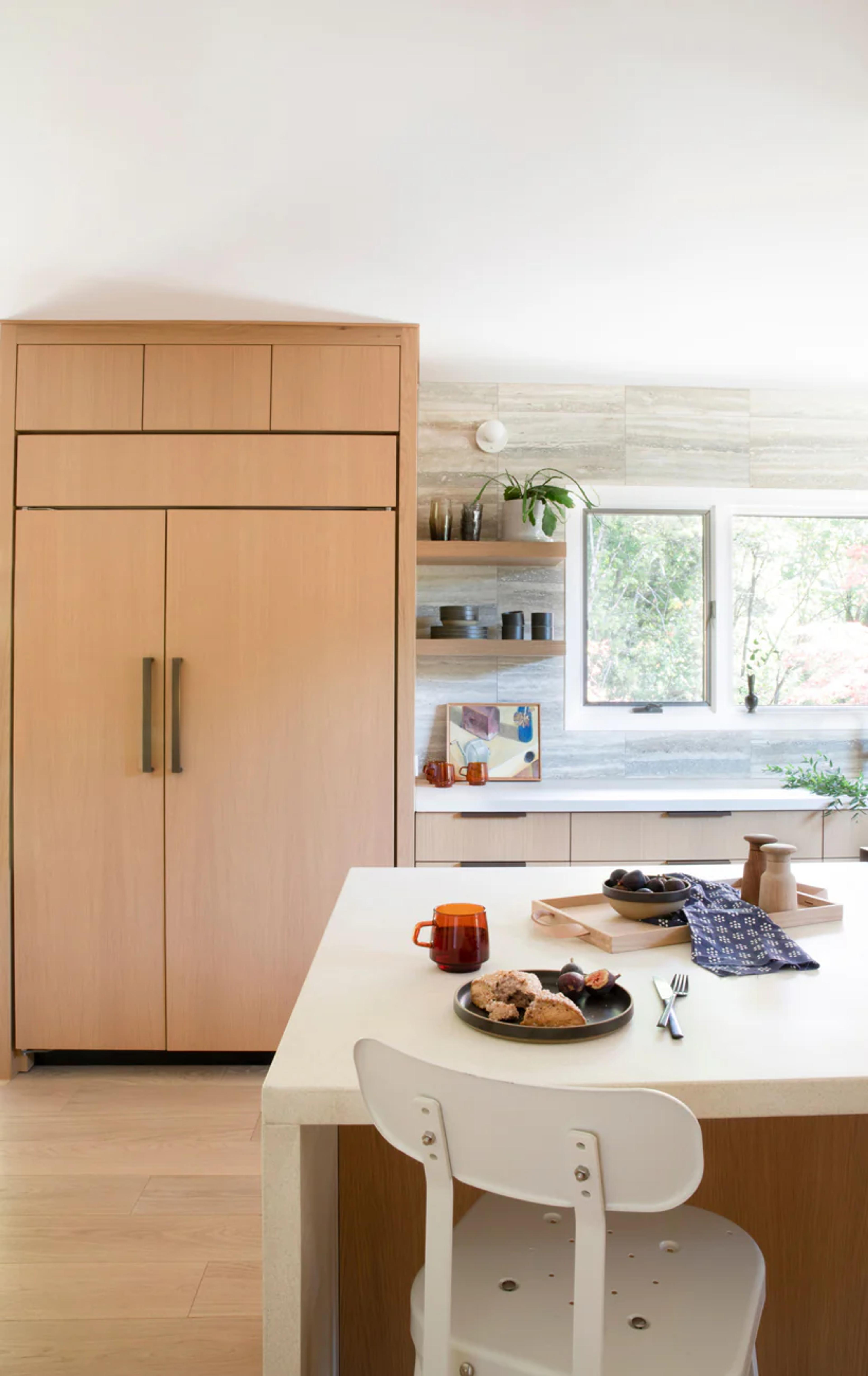 A light filled kitchen with white counters and a tan fridge.