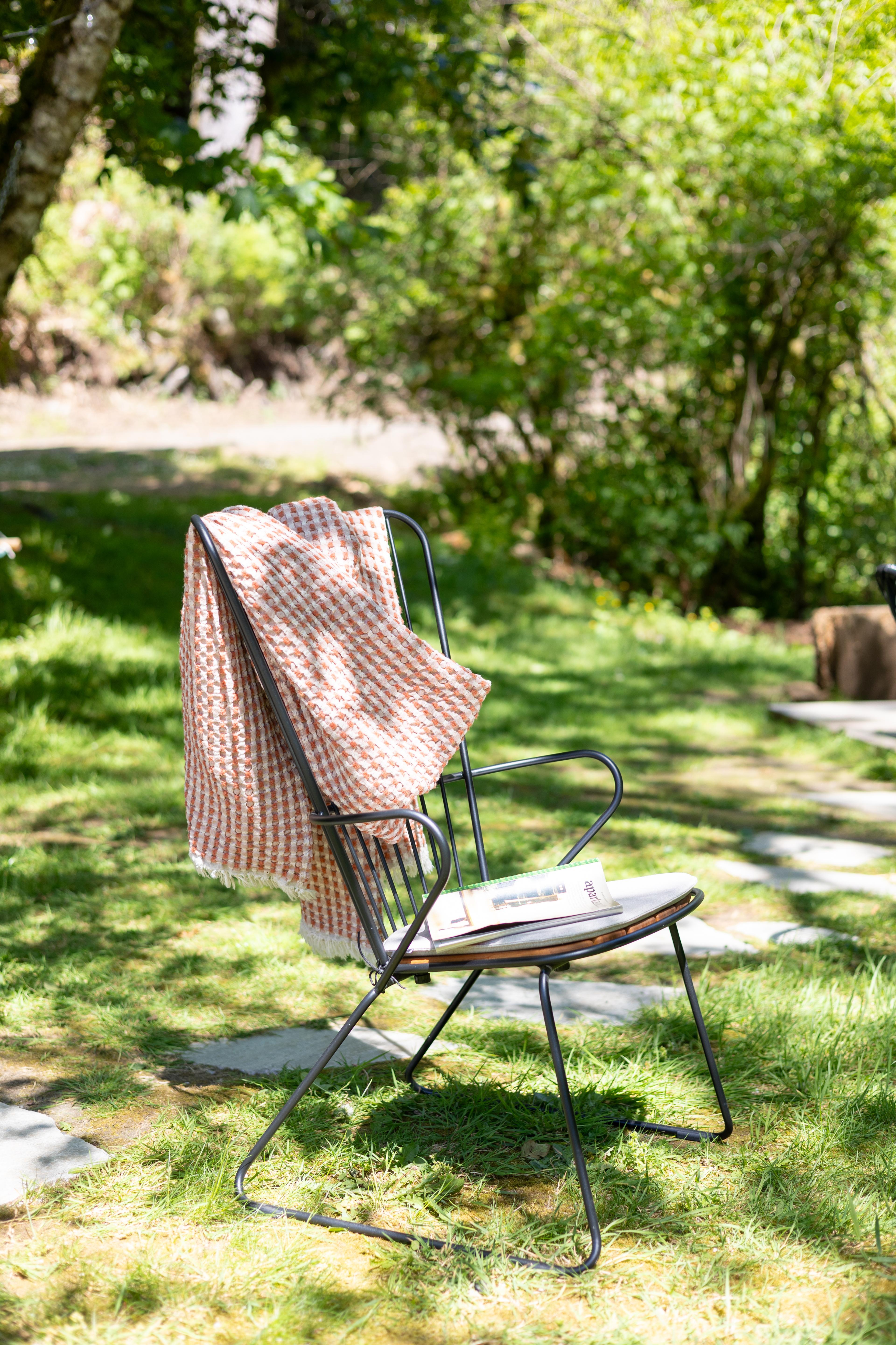 Black chair outside with pink throw blanket slung over it.