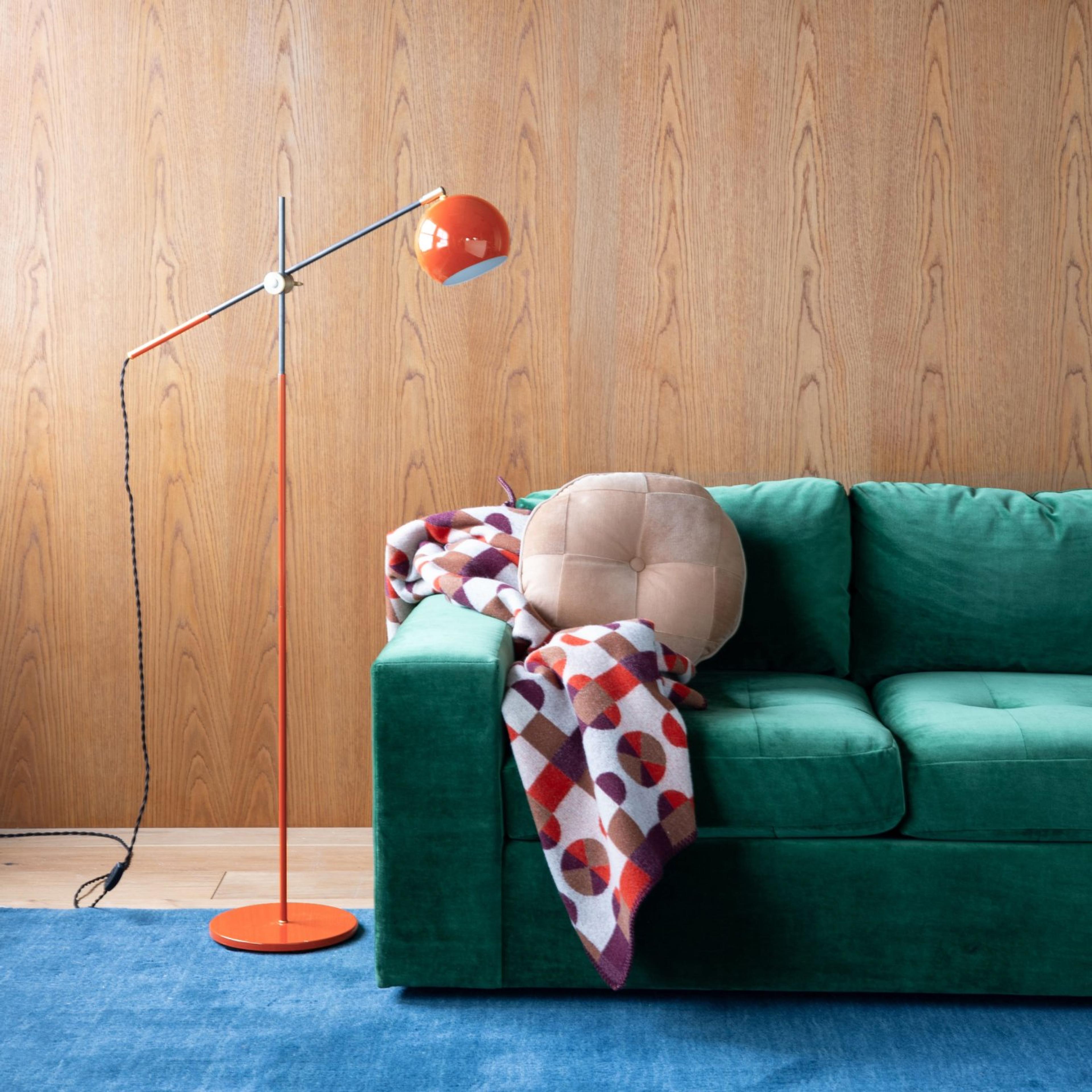 Green velvet couch with a red reading lamp beside it