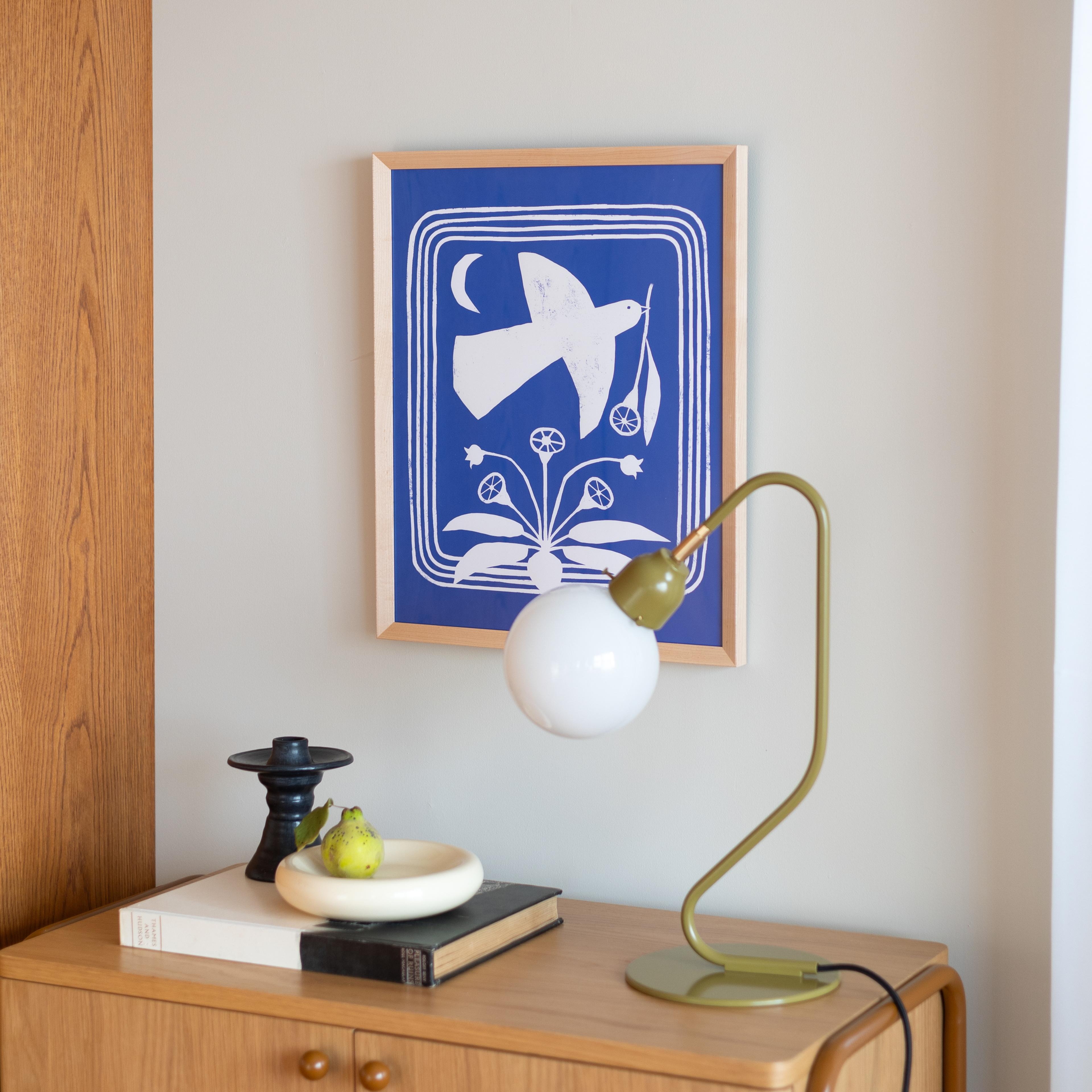 Blue print of bird above cabinet with book and green lamp