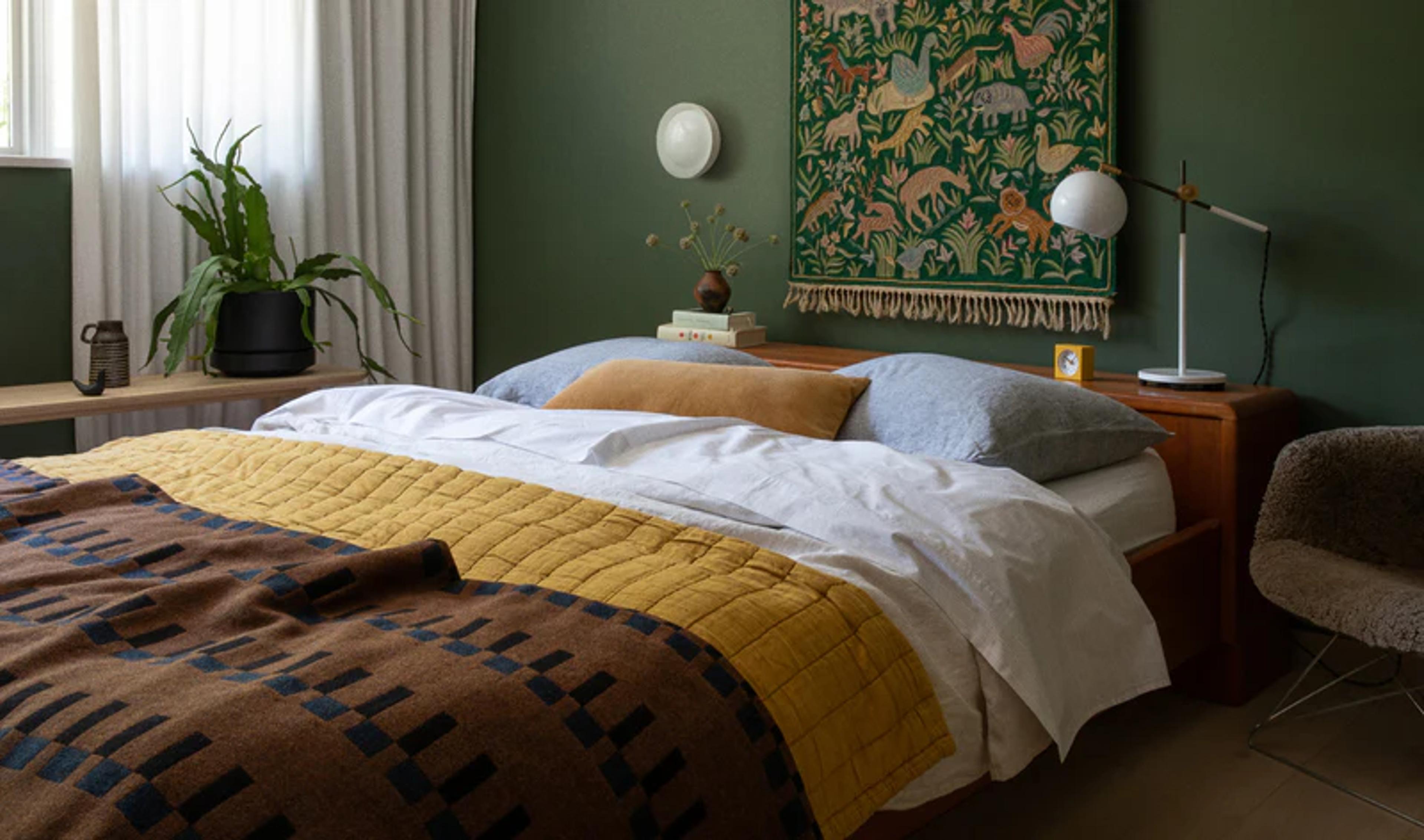 A bedroom with green walls, a forest tapestry, and an earth tone quilt