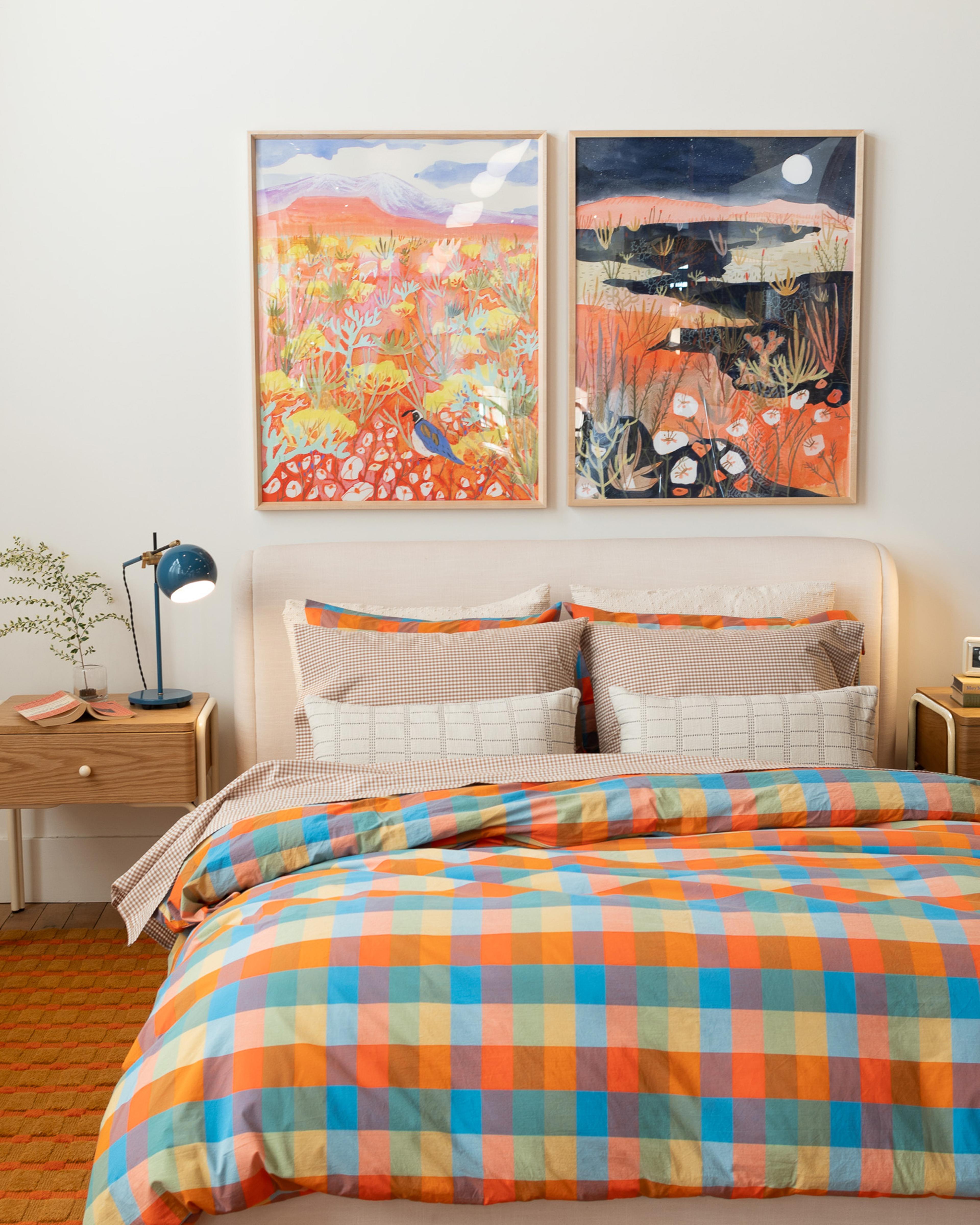 Bed with colorful plaid duvet cover and artists prints above bed 