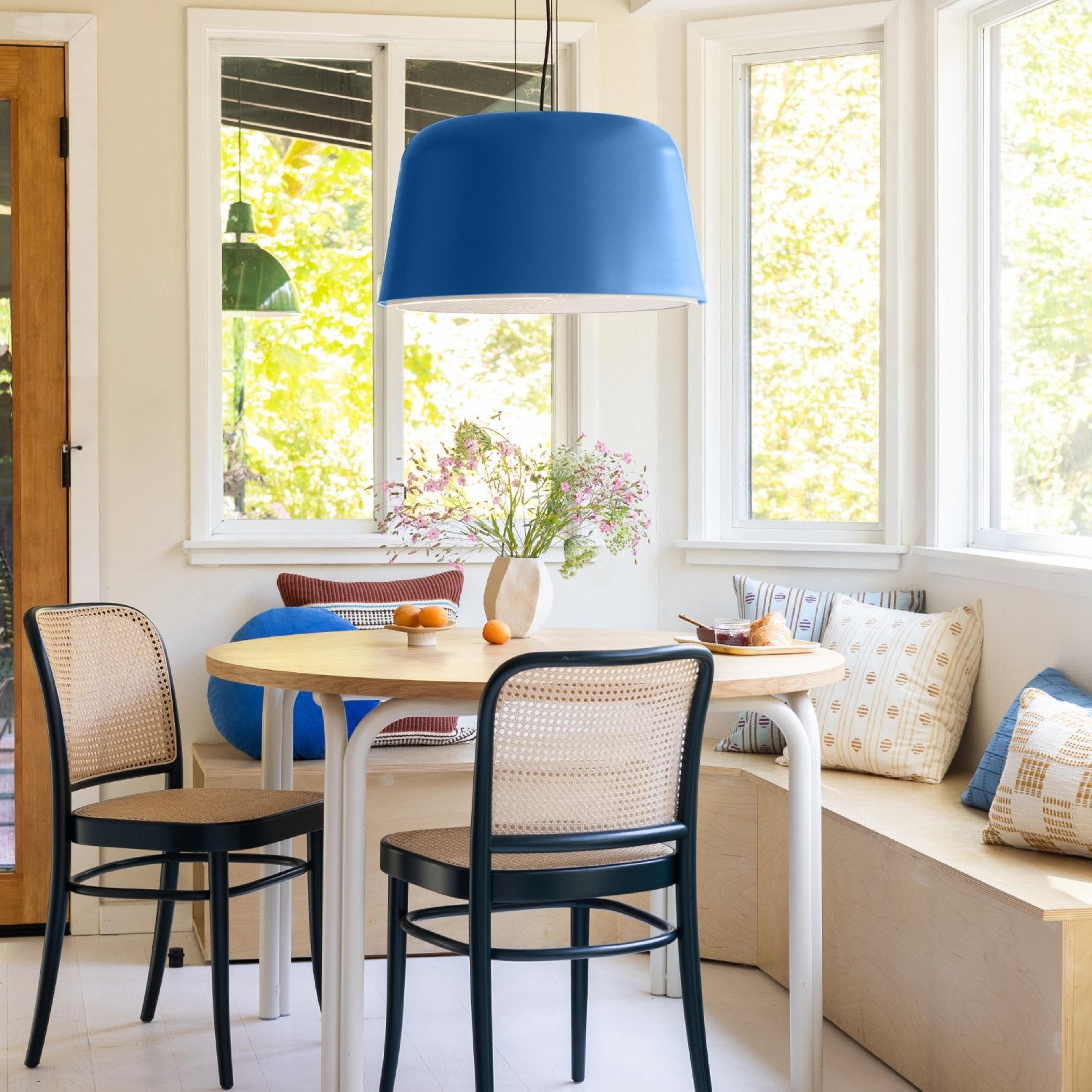 Sunny corner dining room with wooden table and wicker chairs, blue pendant lamp